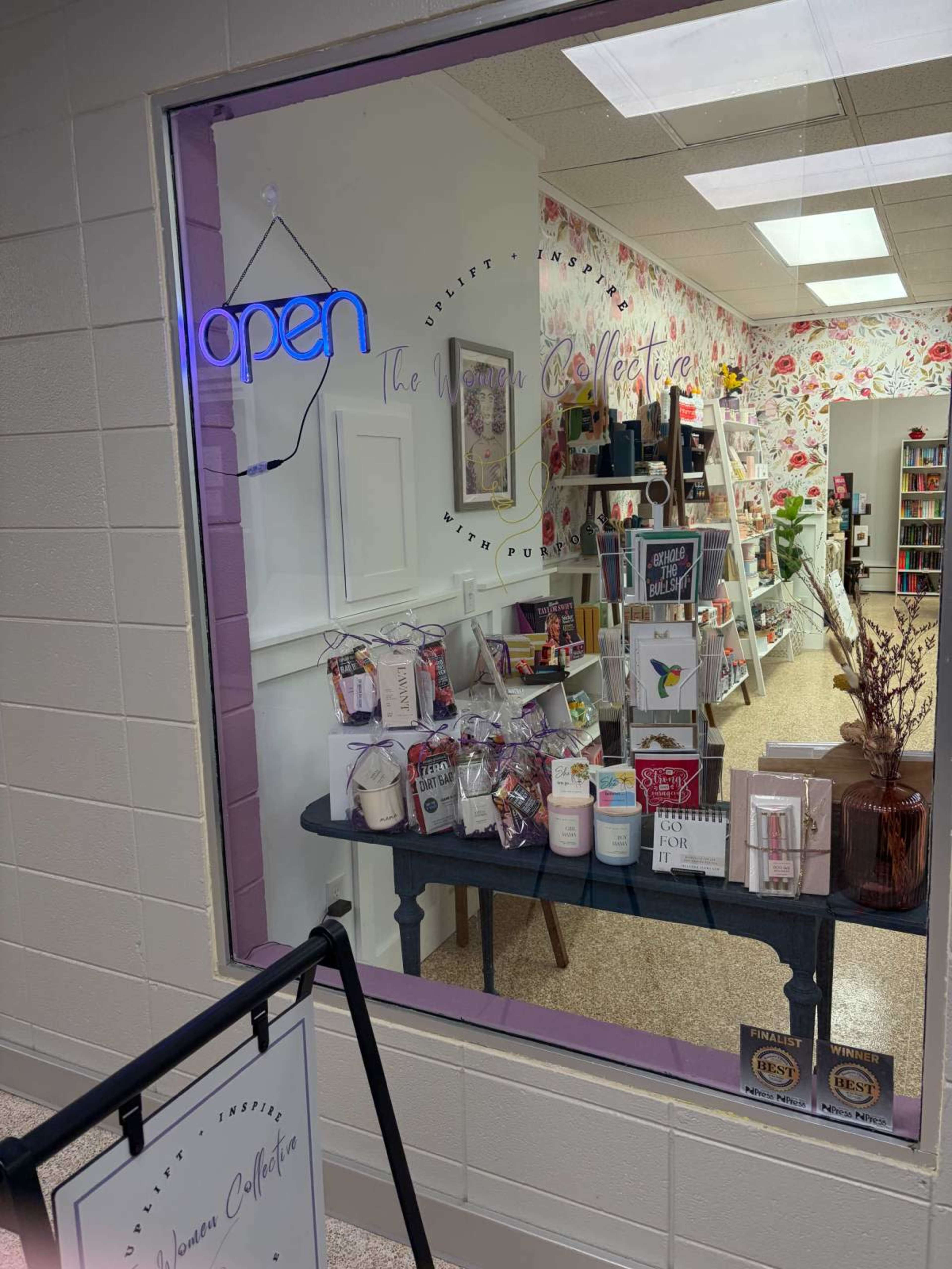 A brightly lit storefront displays a collection of home goods and decor items, along with a neon "open" sign in the window.