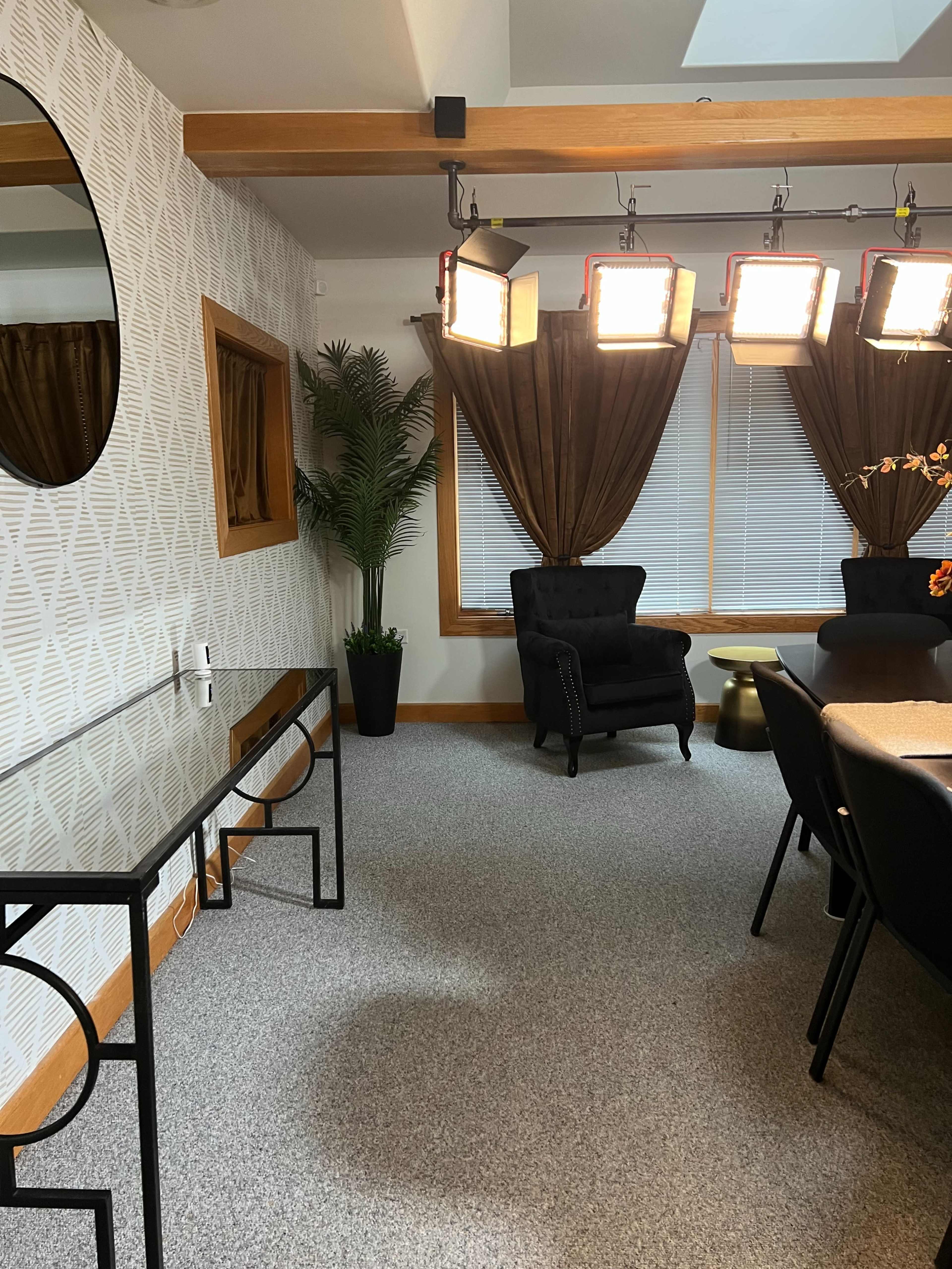 A well-lit room with a black chair near a table, surrounded by decorative curtains and a potted plant.