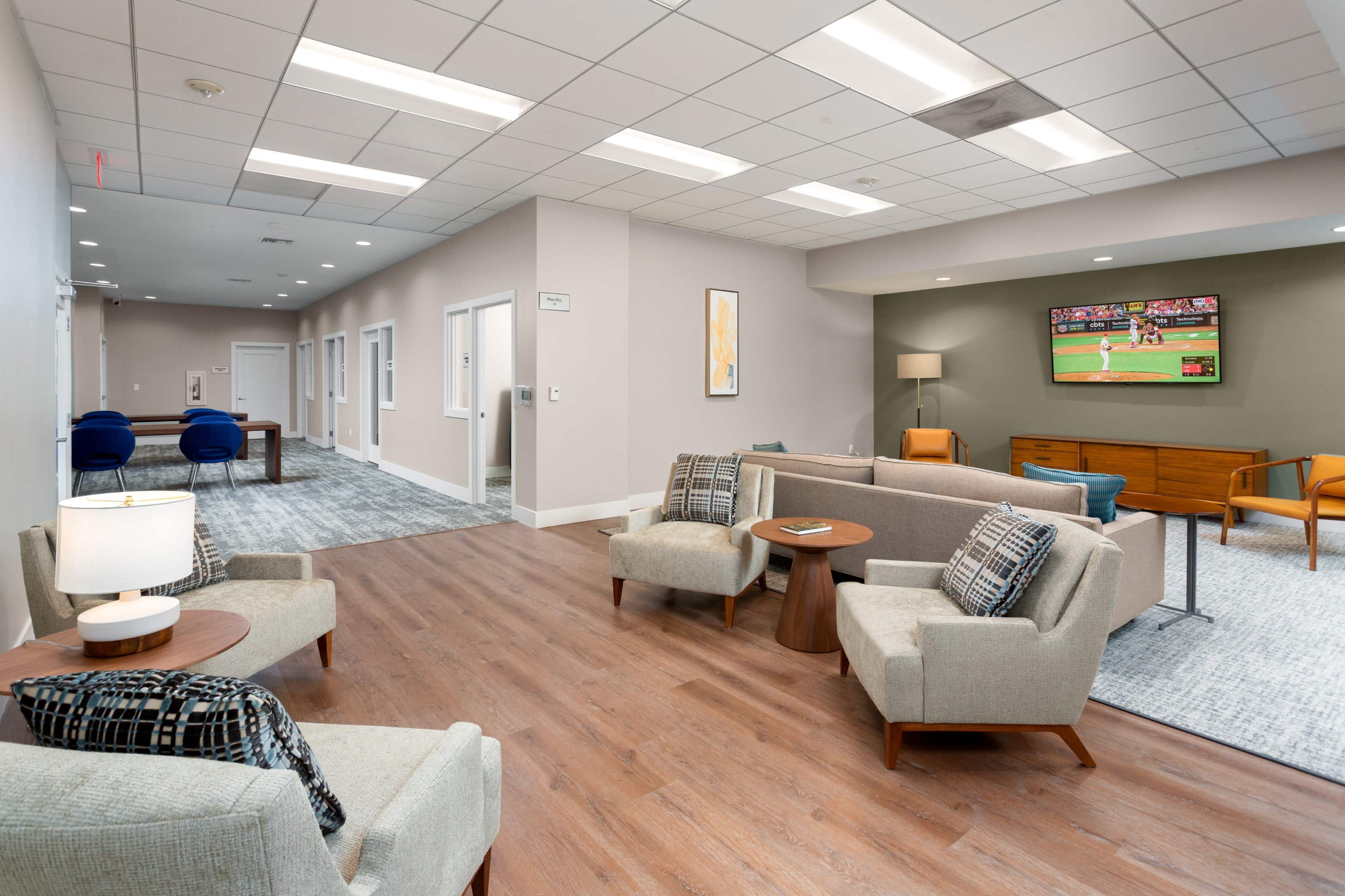 A modern lounge area with comfortable seating arrangements, a television displaying a sports game, and various decorative elements.