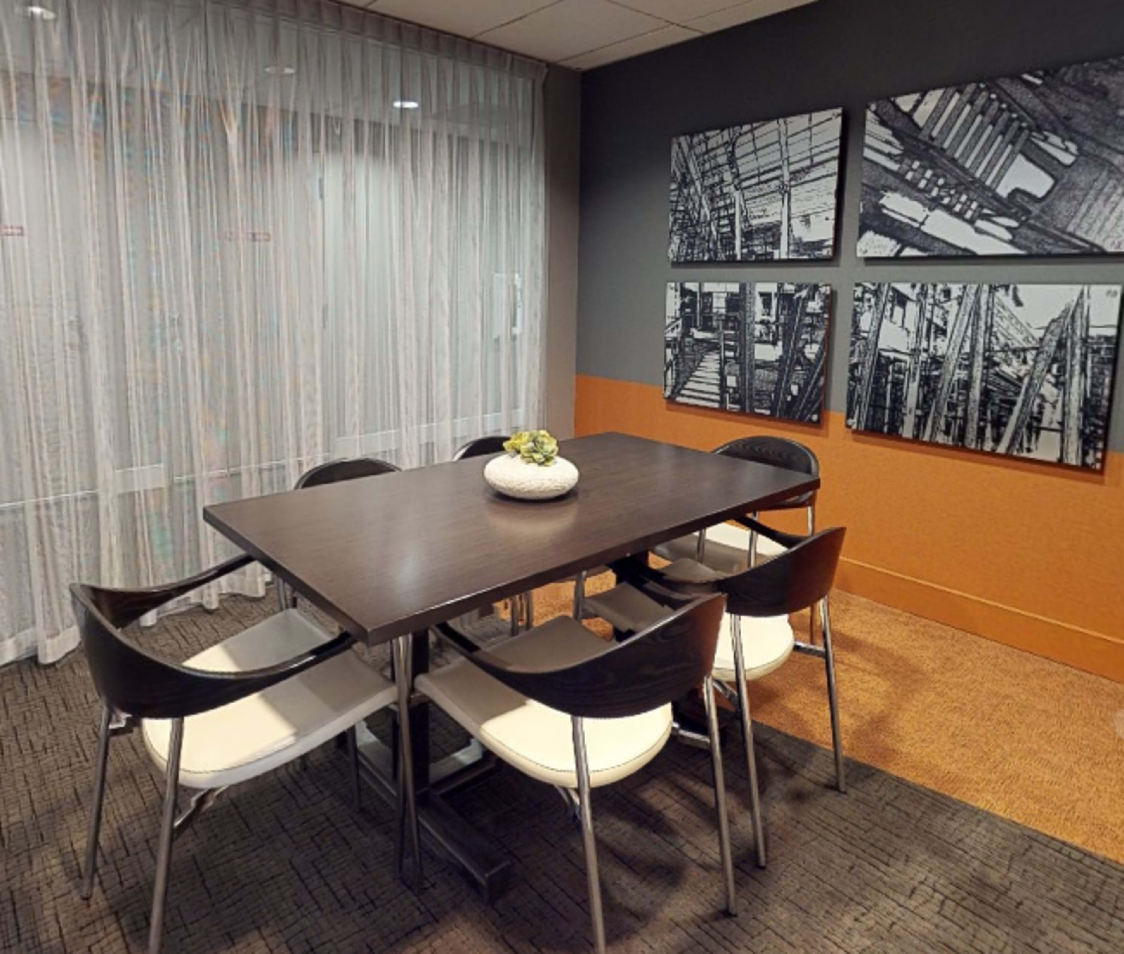 A modern conference room features a rectangular table surrounded by six chairs and decorated with a potted plant, along with framed black-and-white photographs on the walls.