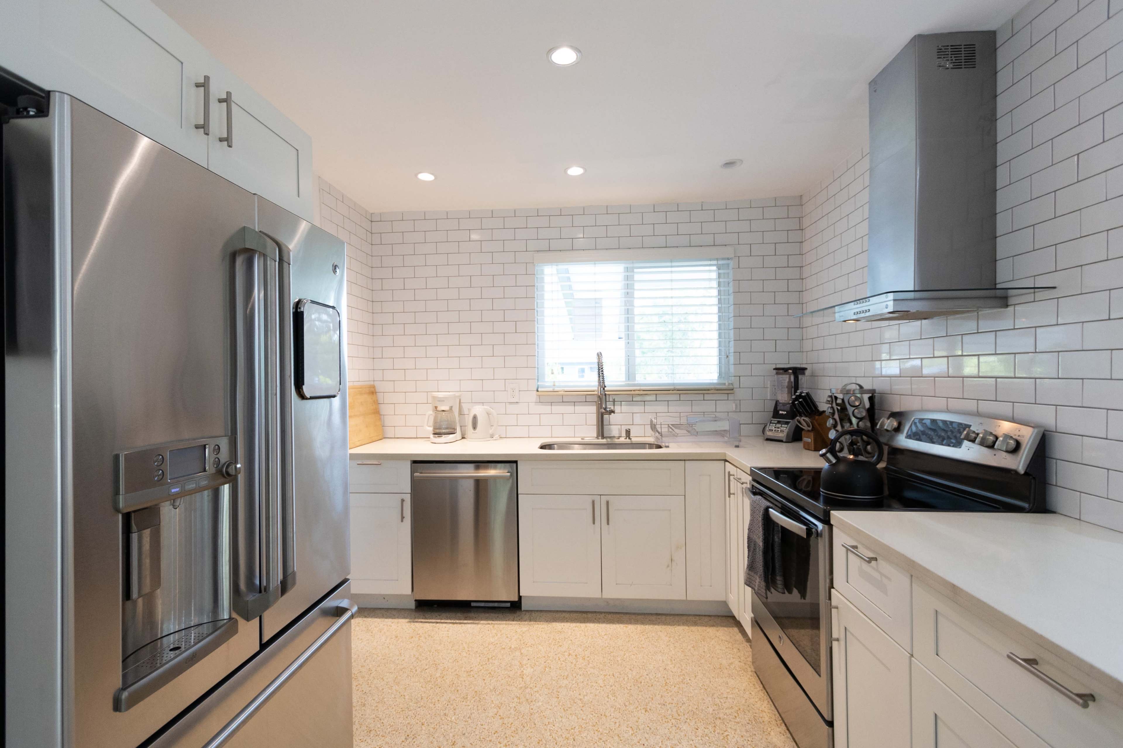 A modern kitchen features stainless steel appliances, white cabinetry, and a tile backsplash with a window providing natural light.