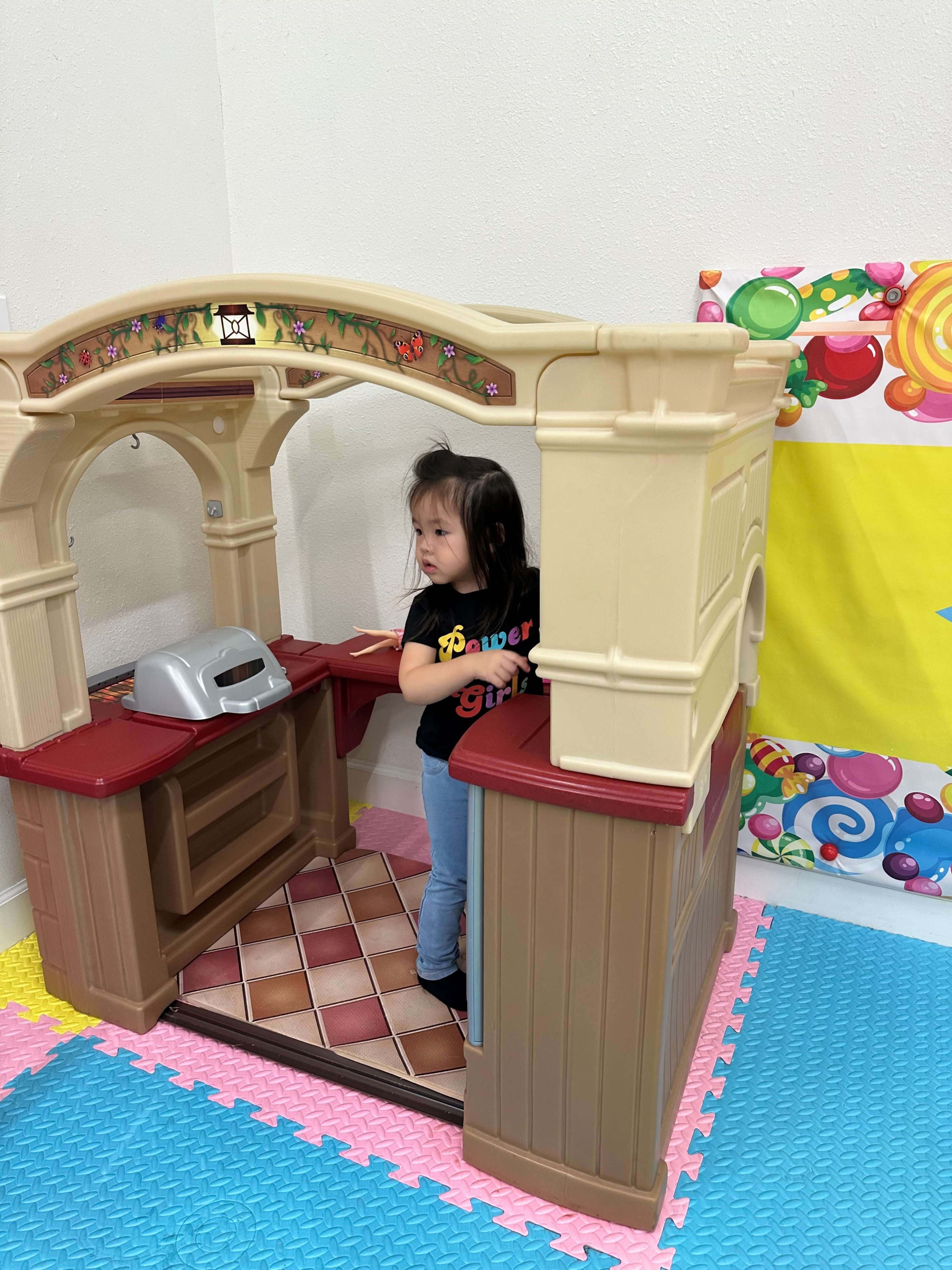 A child is playing inside a plastic toy kitchen set.