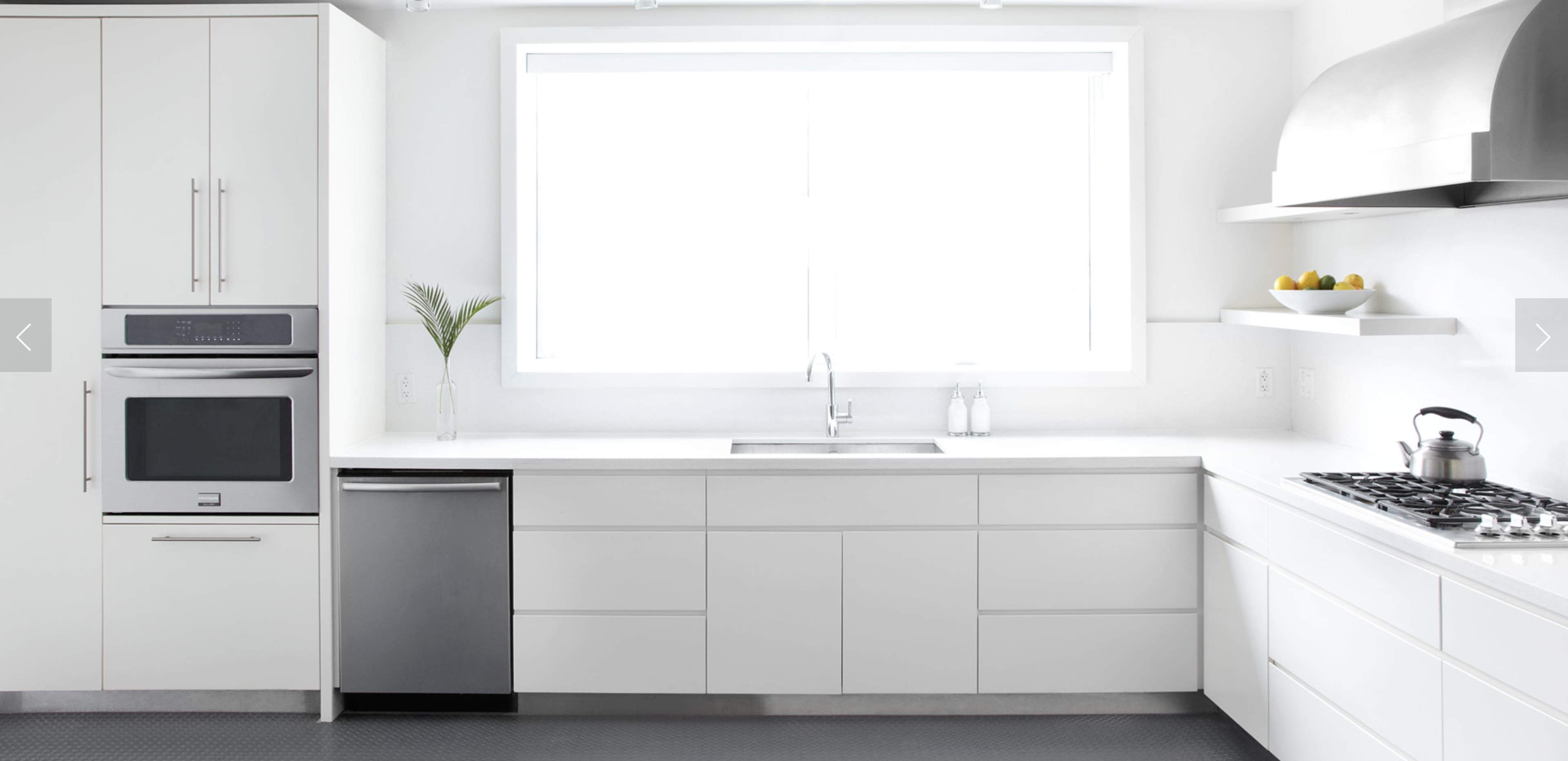 A modern kitchen features white cabinetry, a large window, stainless steel appliances, and a sleek countertop.