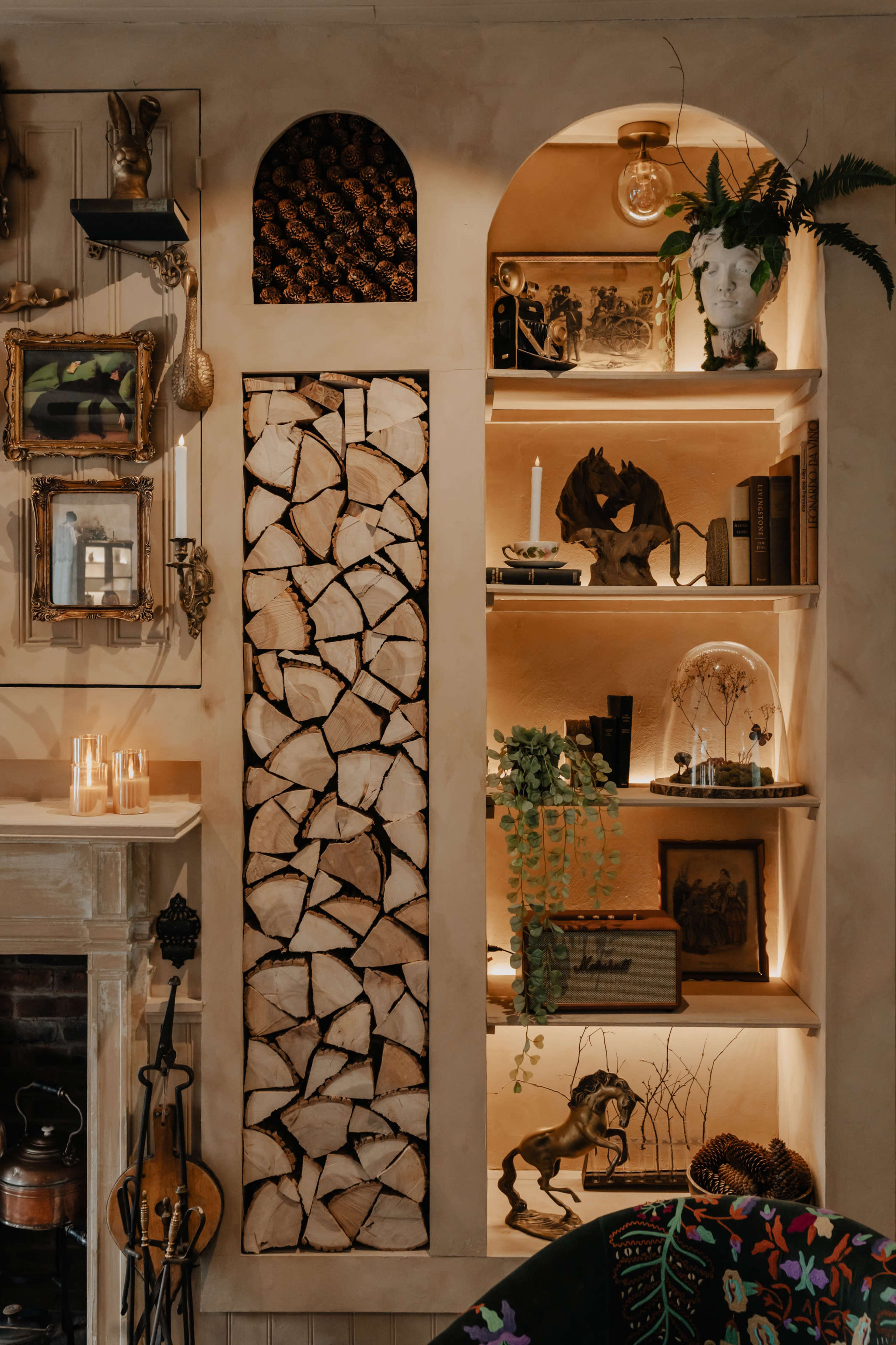 The image shows a well-organized shelving unit with decorative items, books, a candle, and stacked firewood, highlighted by warm lighting.