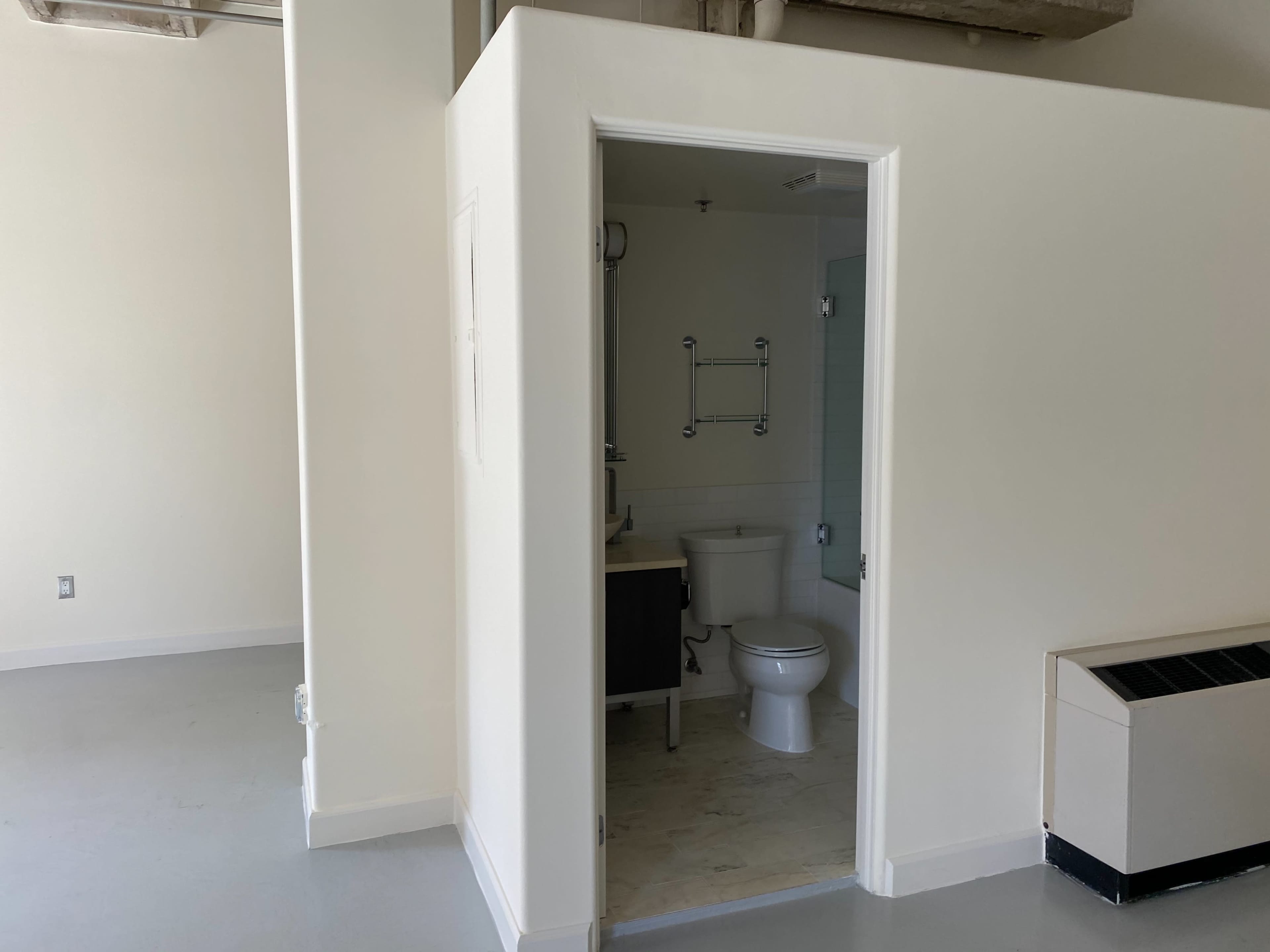 The image shows a clean, empty room with a bathroom area partially visible on the left.