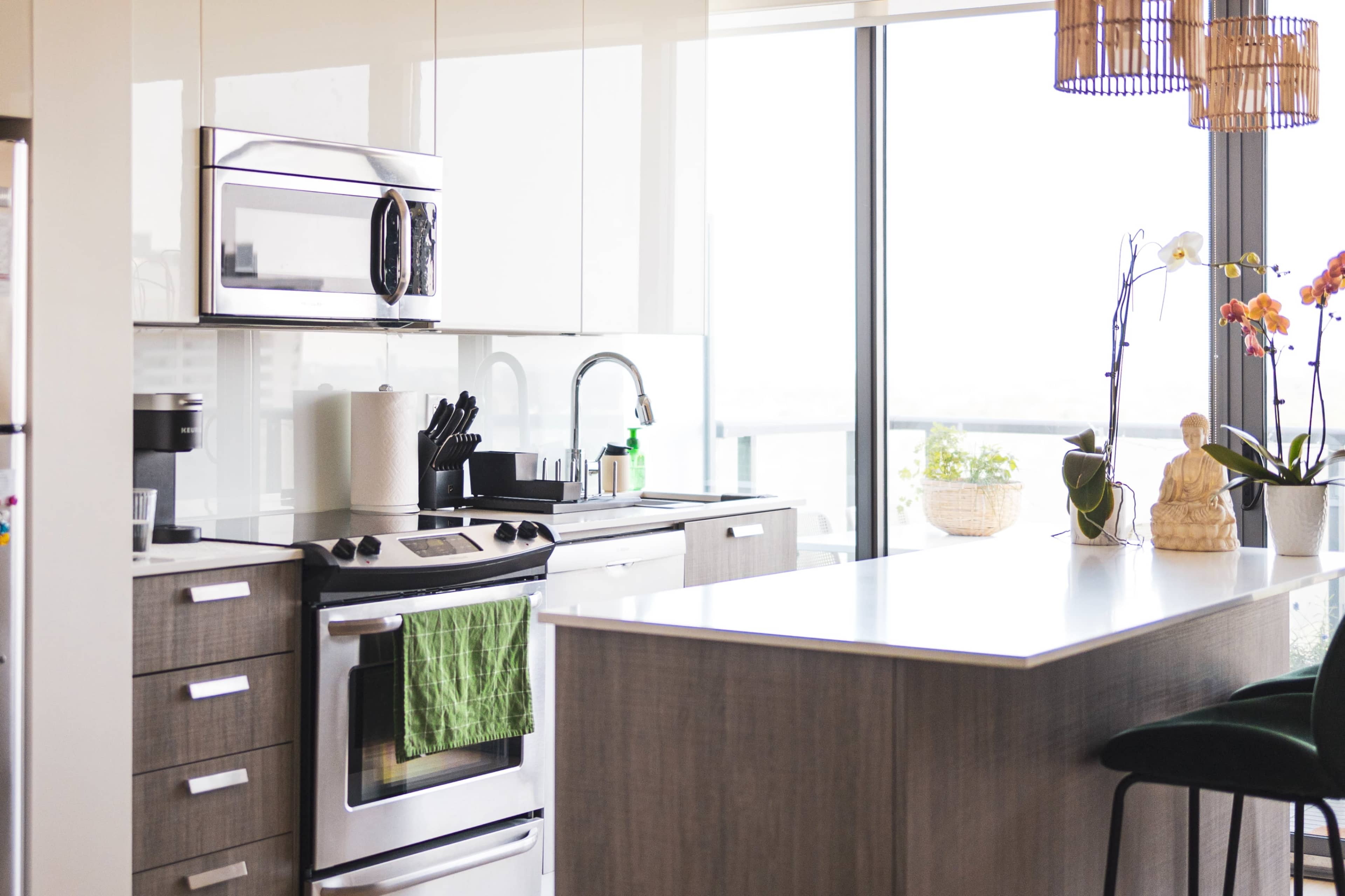 A modern kitchen with stainless steel appliances, a green dish towel hanging from the oven, and a large window providing natural light.