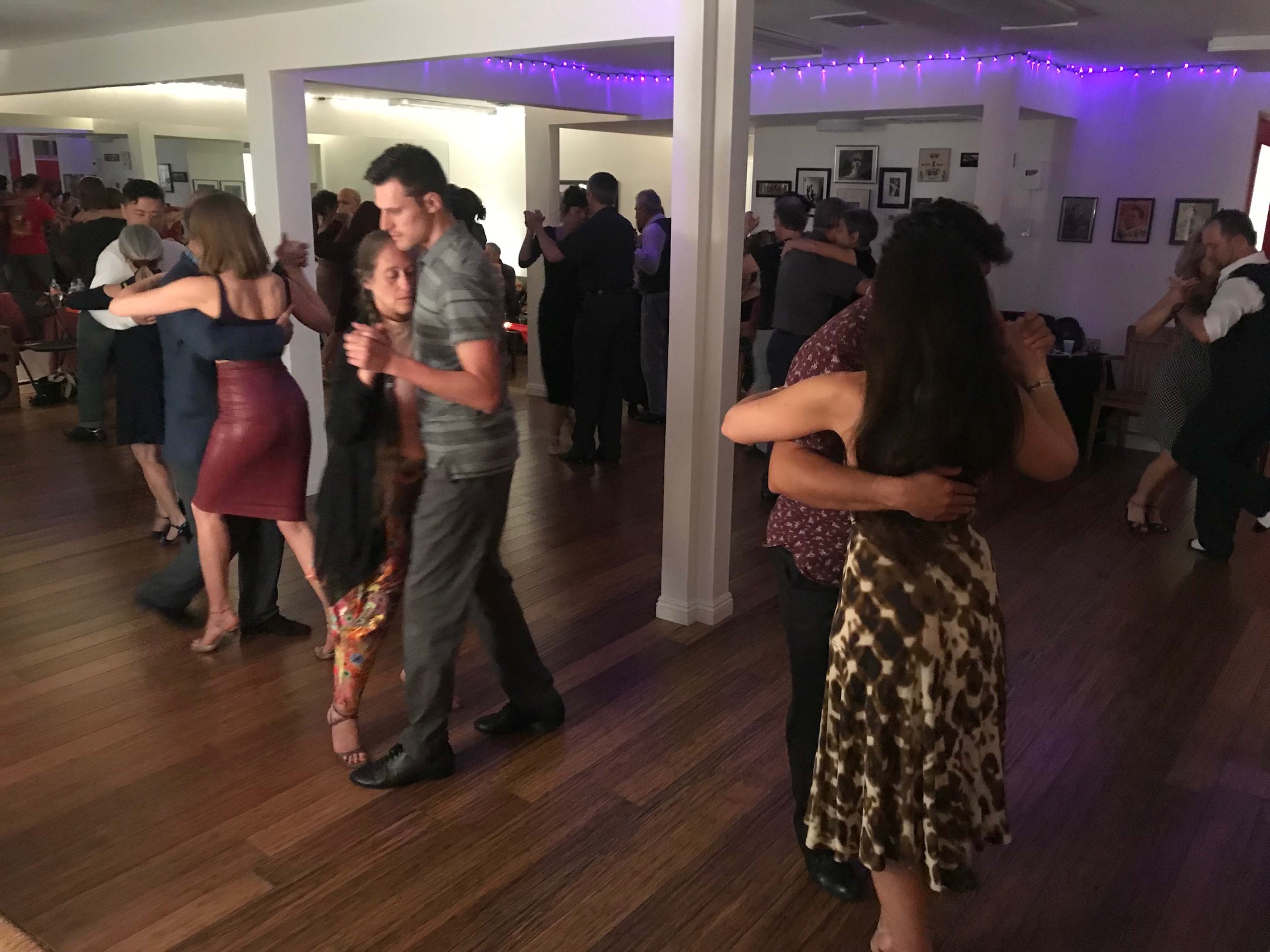 A group of couples are dancing closely in a well-lit social dance hall.