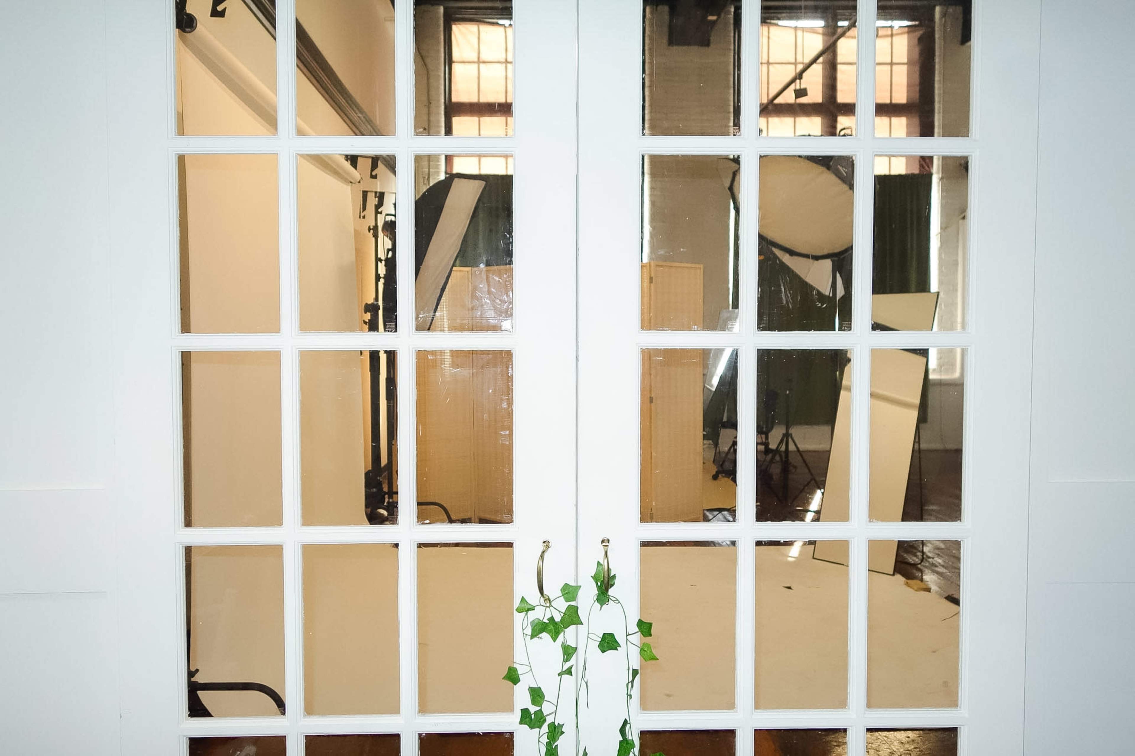 The image shows a set of double doors with large glass panes, providing a view into a photography studio equipped with lighting and a backdrop.