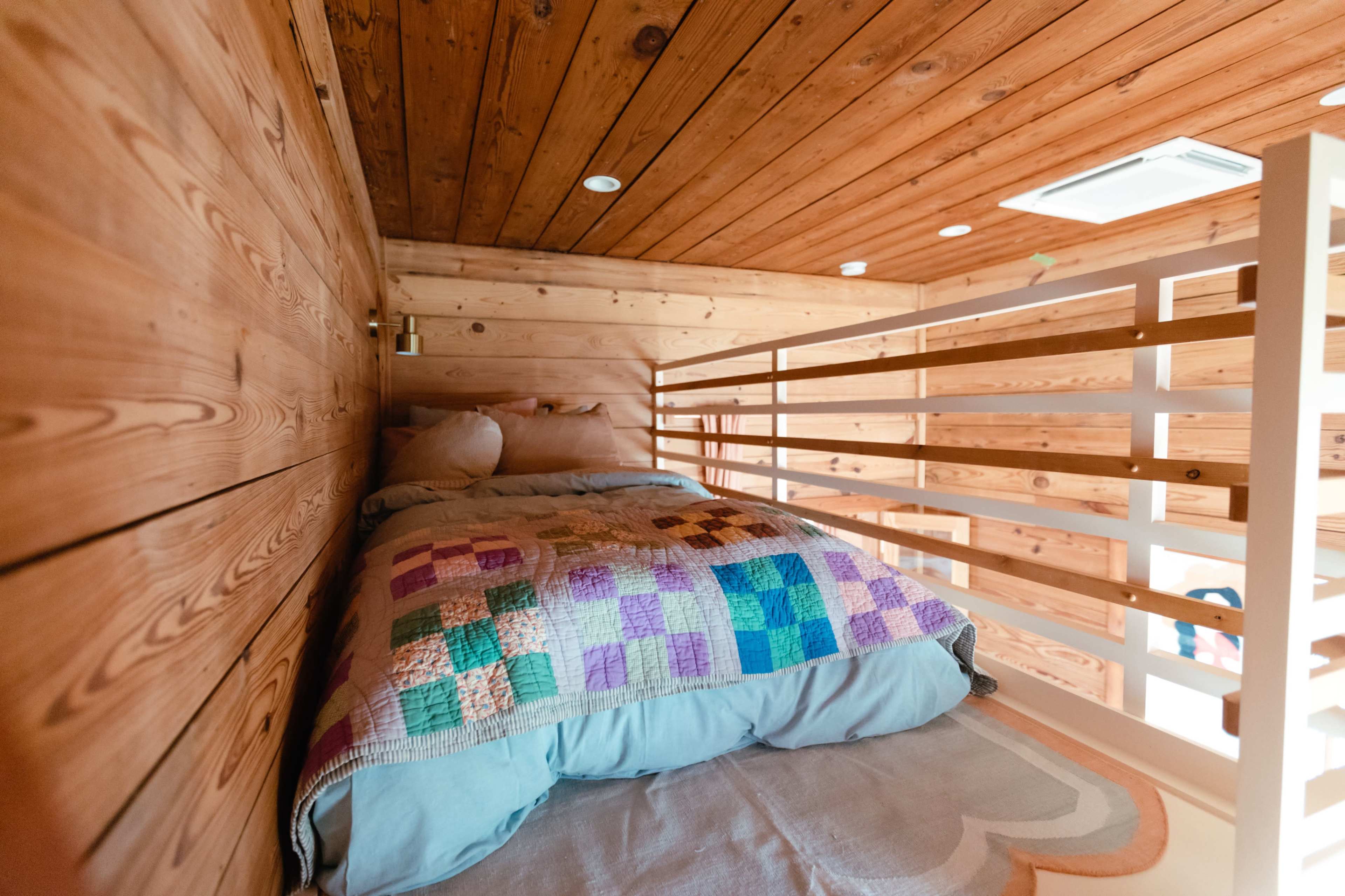 A cozy lofted sleeping area features a bed with a patchwork quilt against a wooden wall.