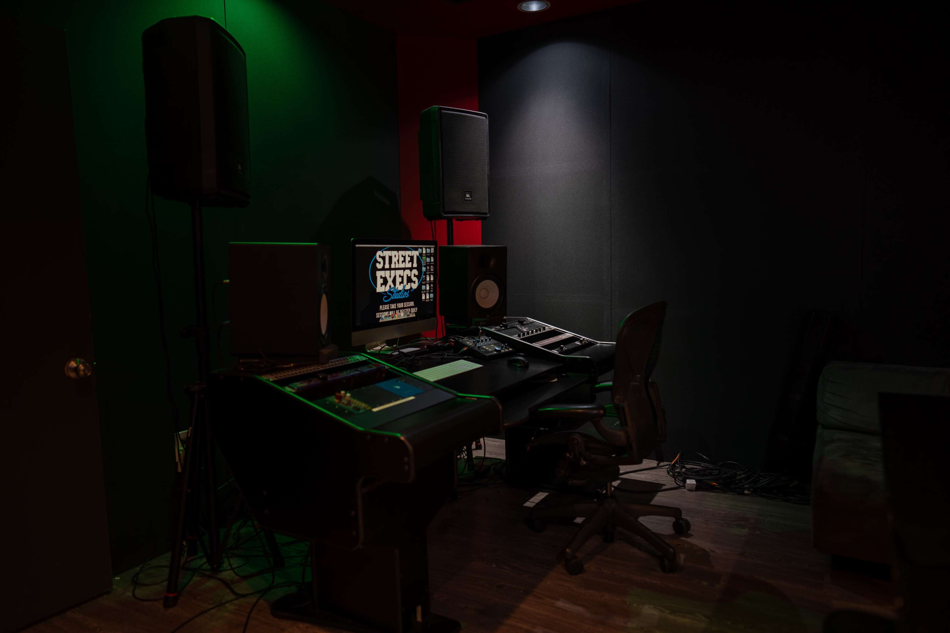 A music production studio featuring a desk with computer equipment, speakers, and soundproofing on the walls.
