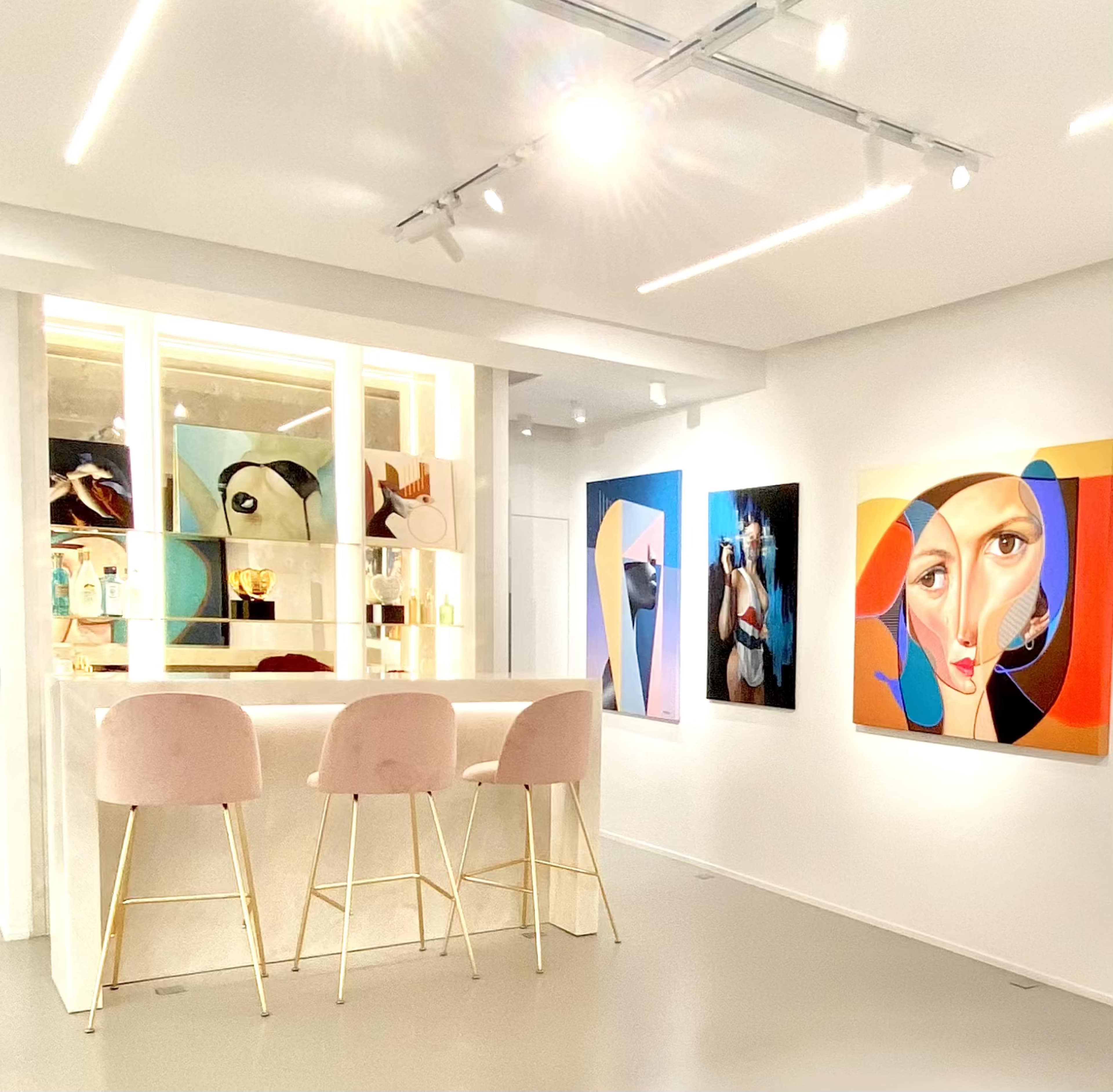 A modern art gallery features a sleek bar with three pink stools, surrounded by colorful contemporary paintings on the walls.