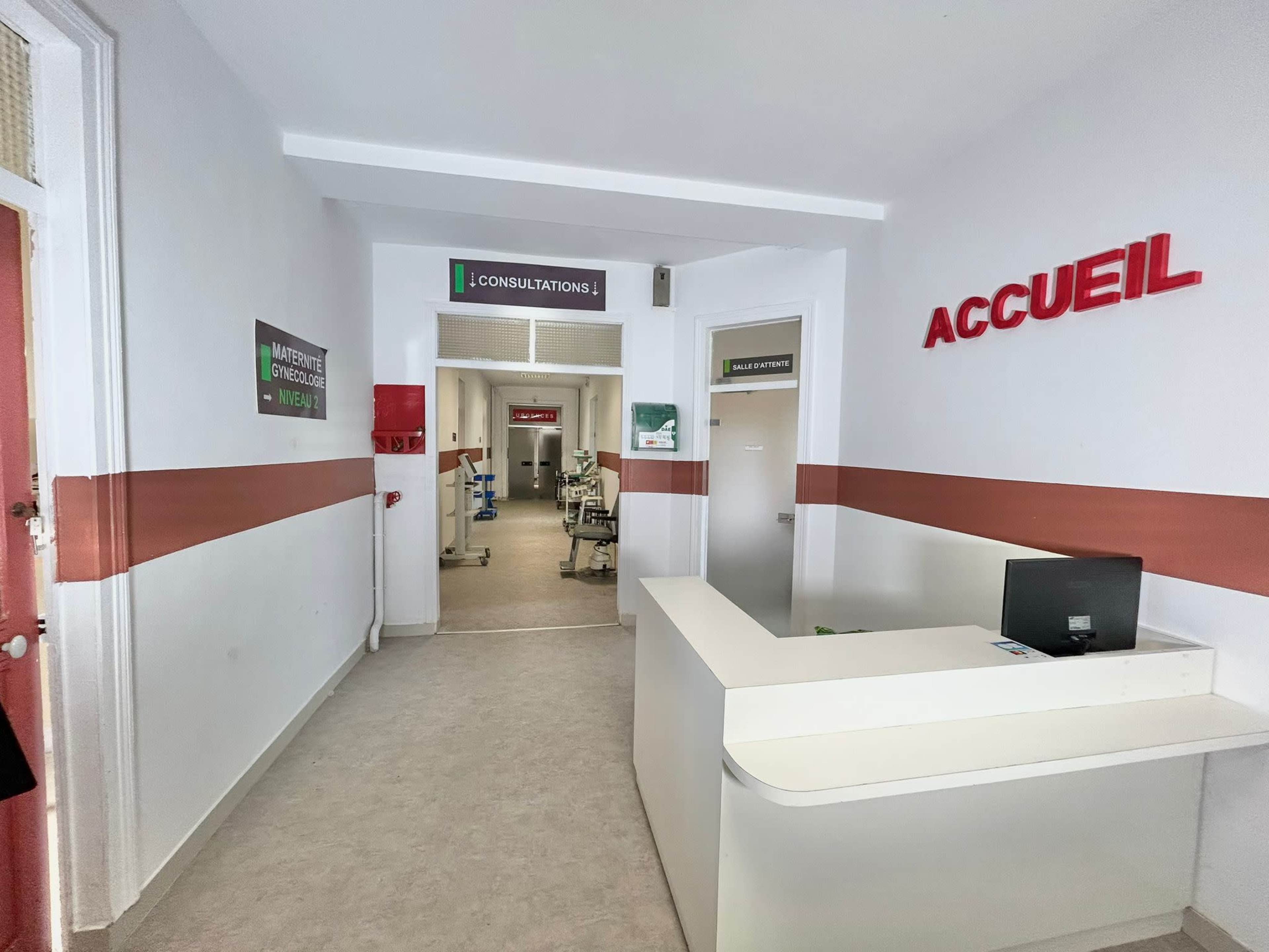 A well-lit hallway in a medical facility with a reception desk on the left and signs indicating consultations ahead.