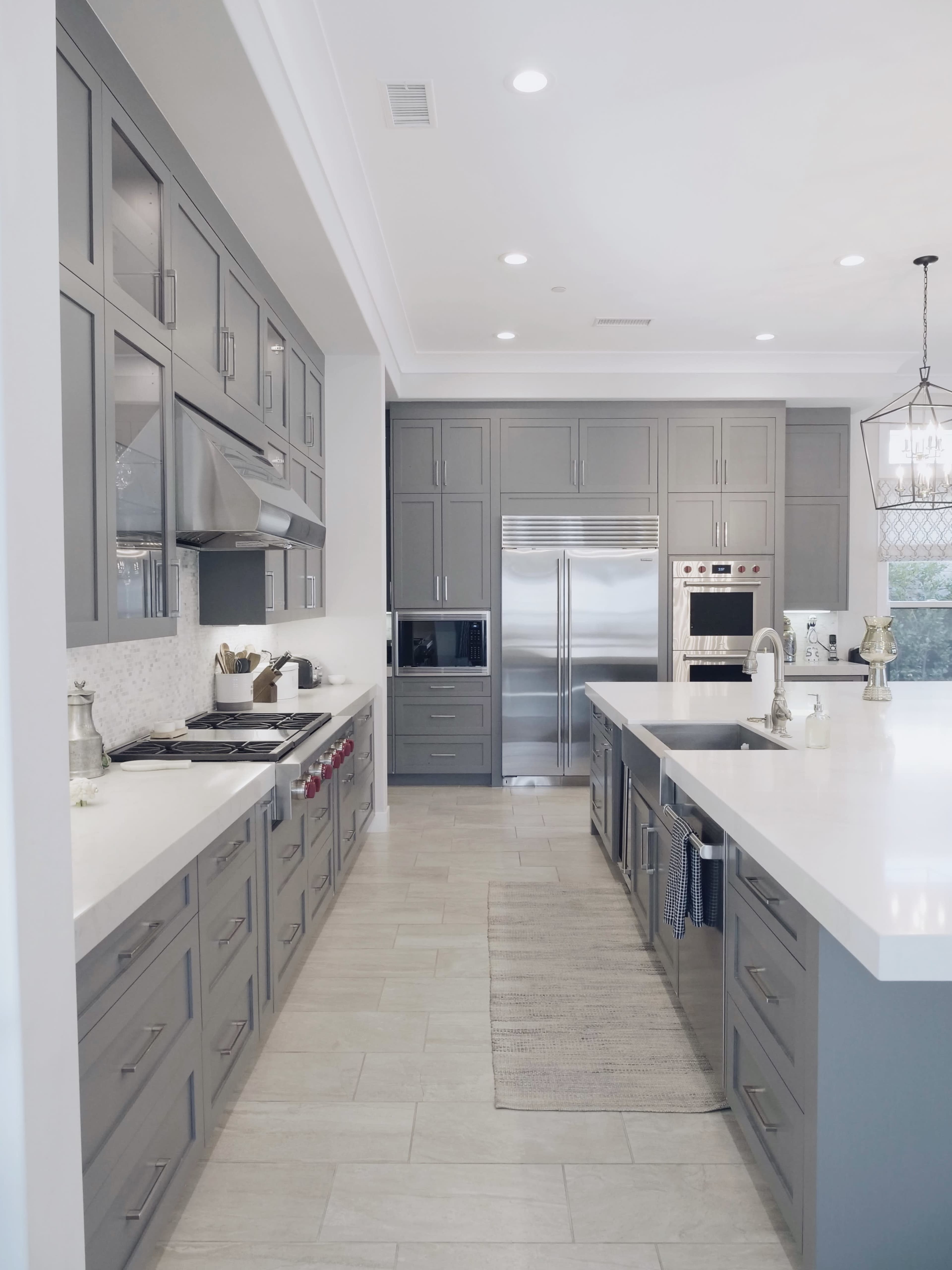 The image shows a modern kitchen featuring gray cabinets, stainless steel appliances, and white countertops.