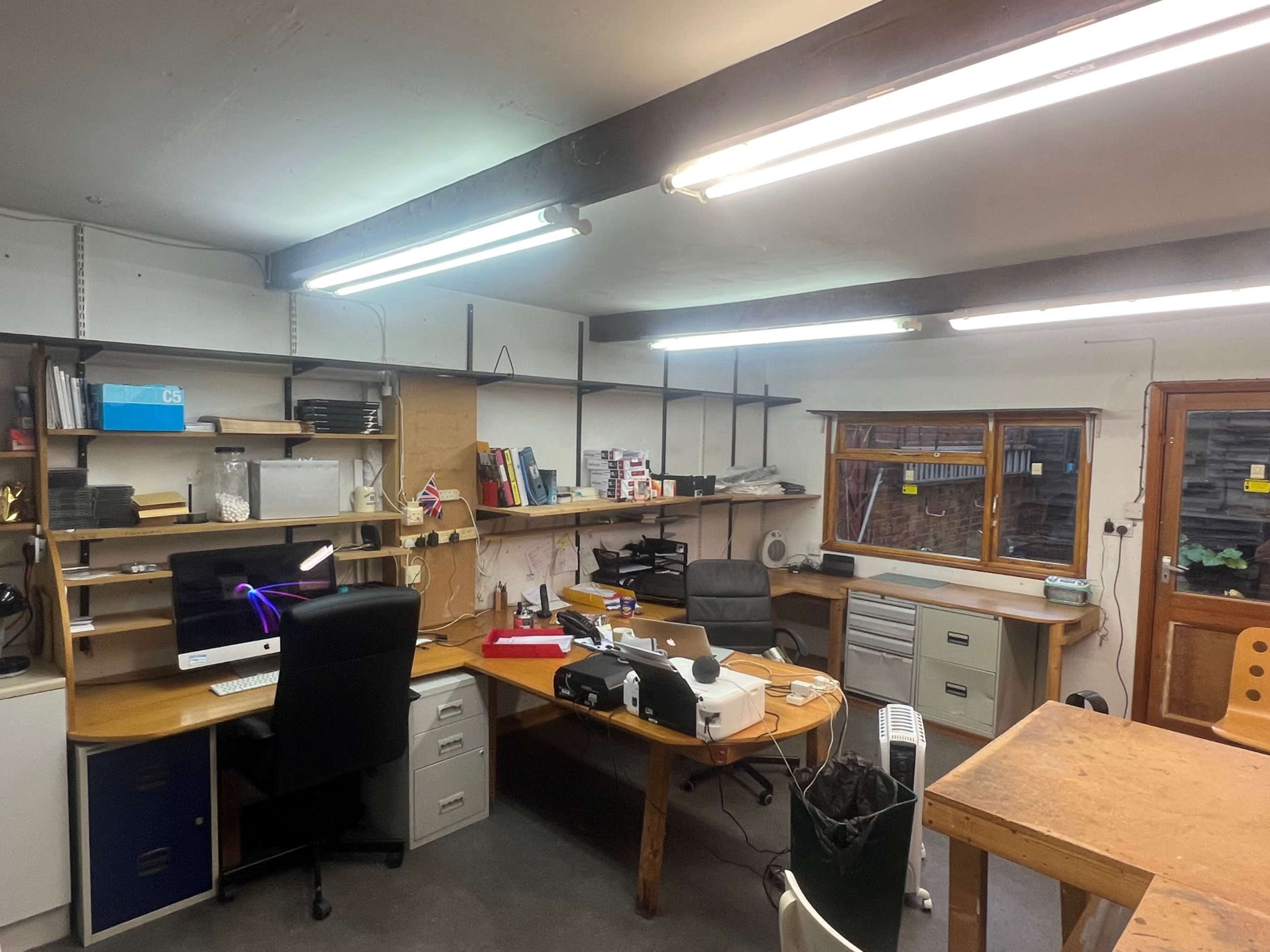 An office space with a desk, computer, shelves, and various office supplies organized against the walls.