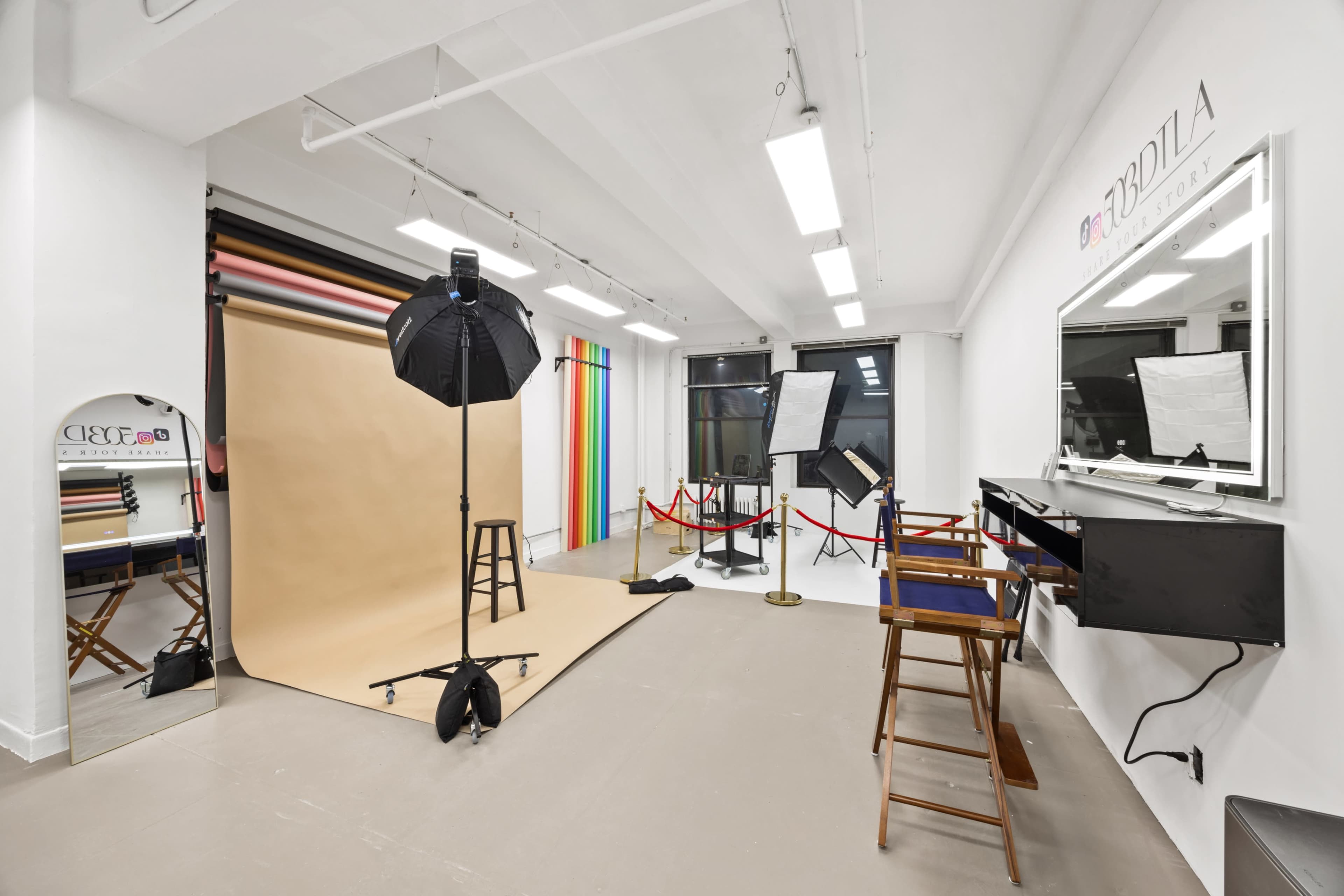 The image shows a photography studio with backdrop stands, lighting equipment, and makeup stations arranged in a spacious room.