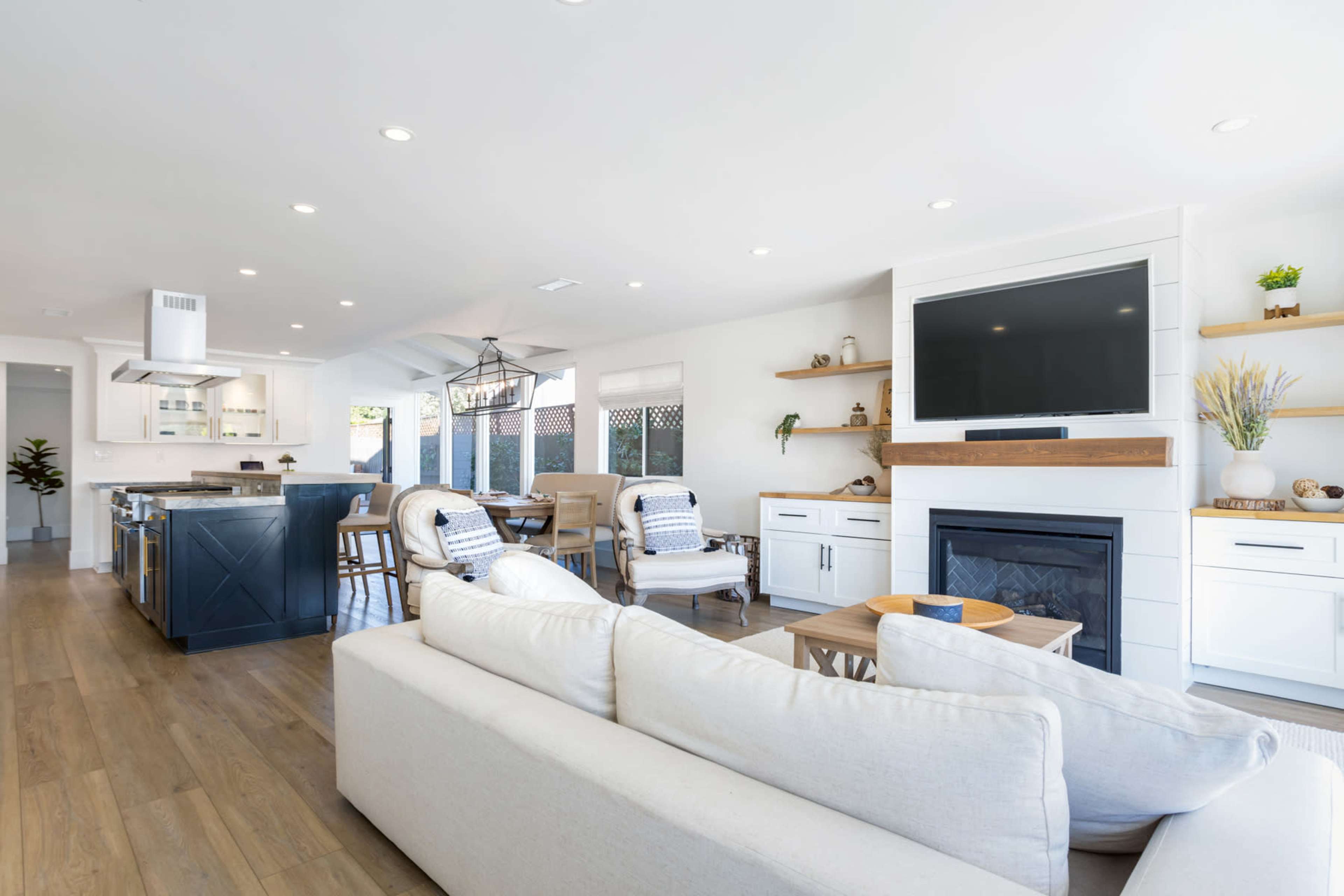 A modern kitchen and living area feature an open layout, with a fireplace, television, and seating arrangements.