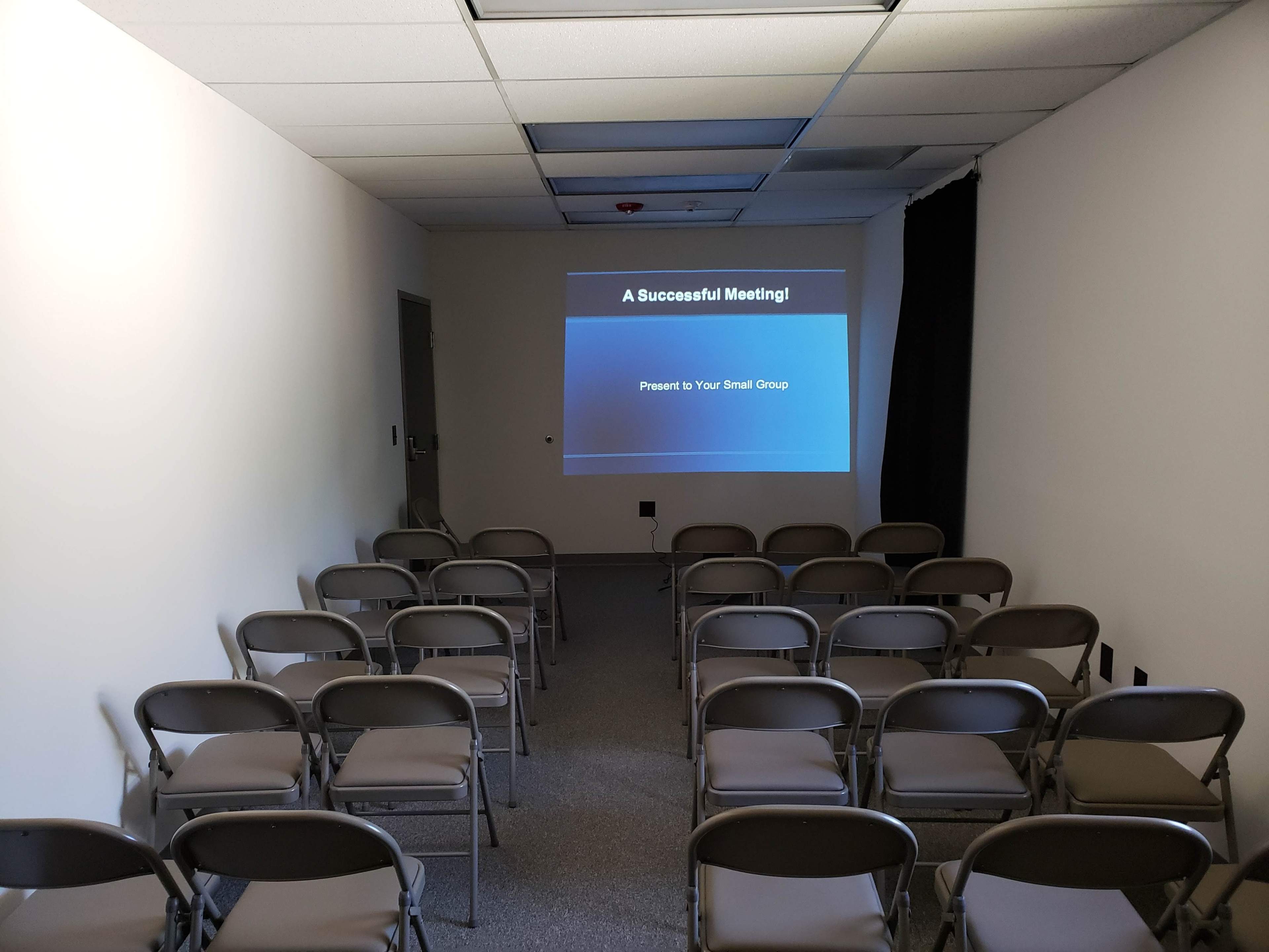 The image shows a small meeting room with rows of folding chairs facing a projector screen displaying the title "A Successful Meeting!"