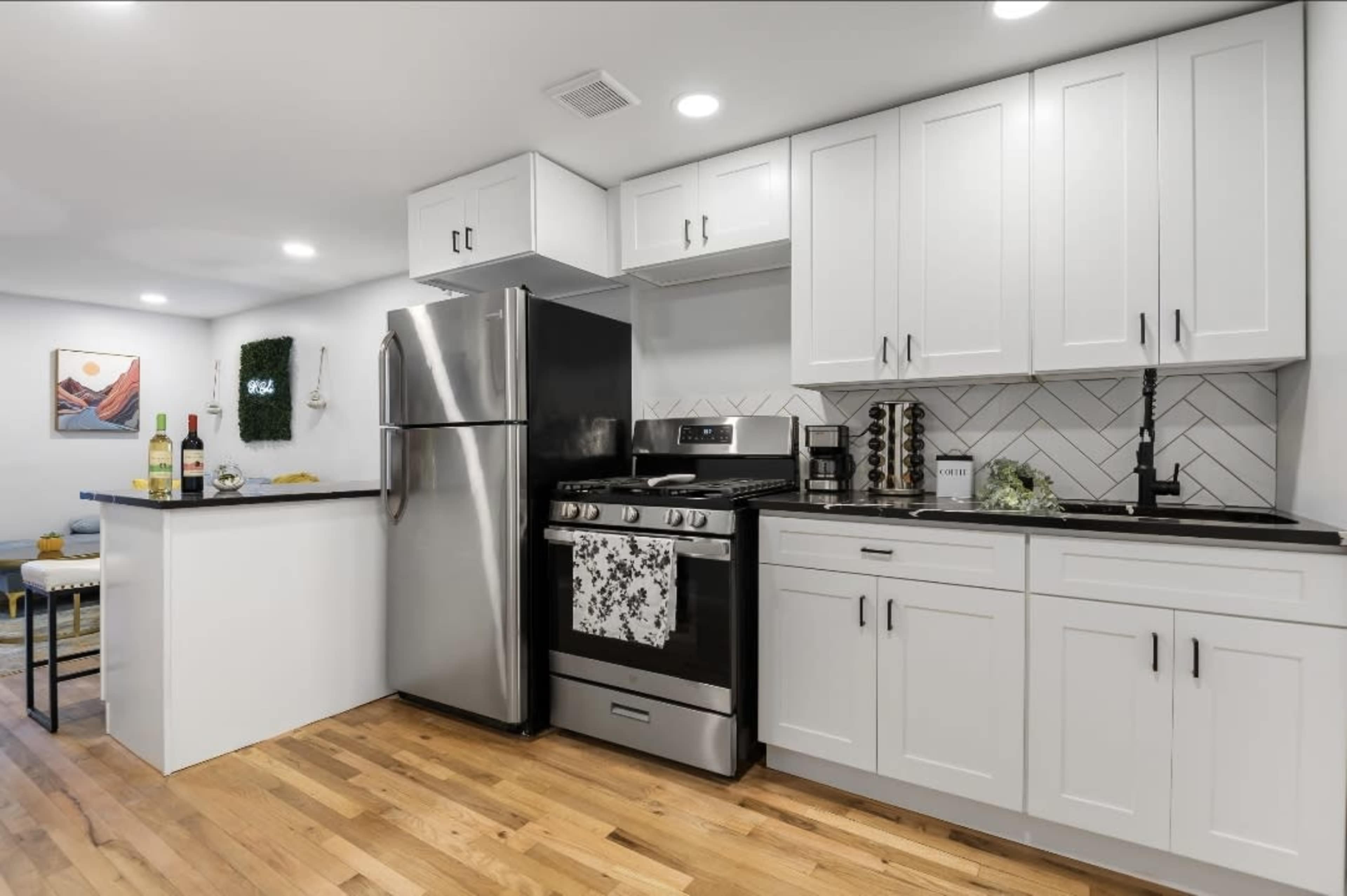 The kitchen features white cabinets, a stainless steel refrigerator, a black stove, and wooden flooring.