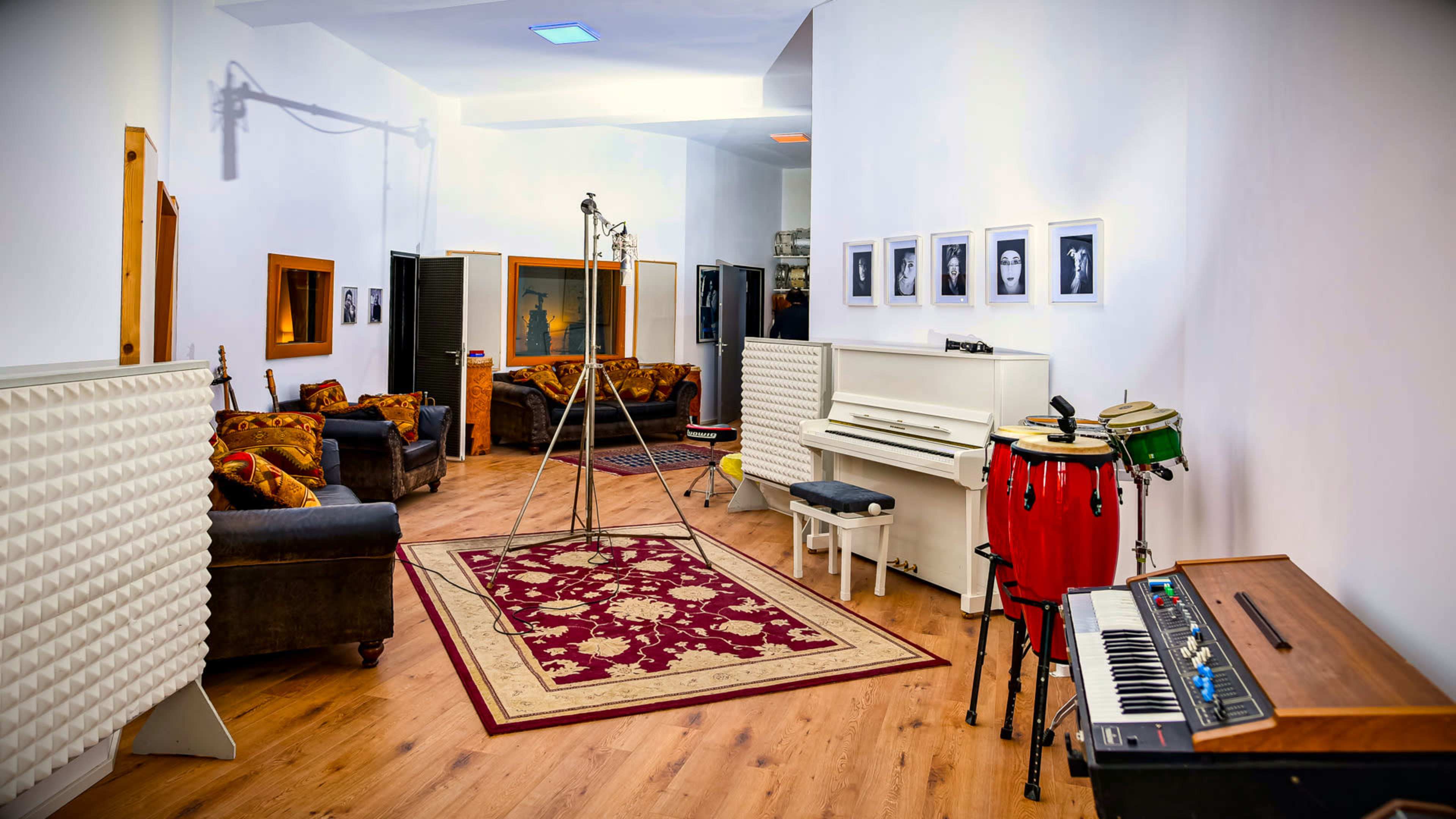 A music studio featuring a cozy lounge area with sofas, a piano, a keyboard, and soundproofing panels on the walls.