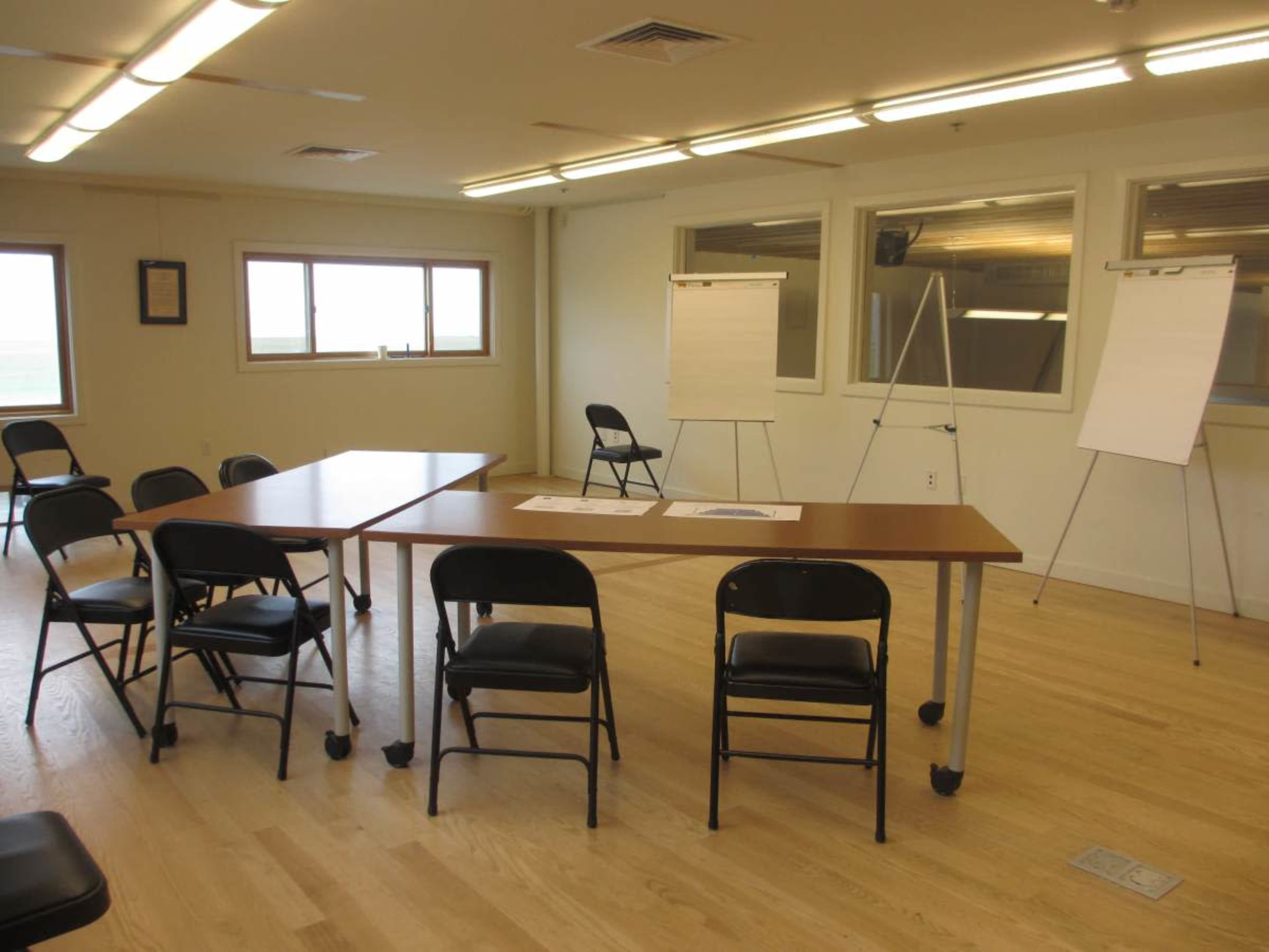 The image shows a meeting room with a long table surrounded by black chairs and three easels holding blank flipcharts against the walls.