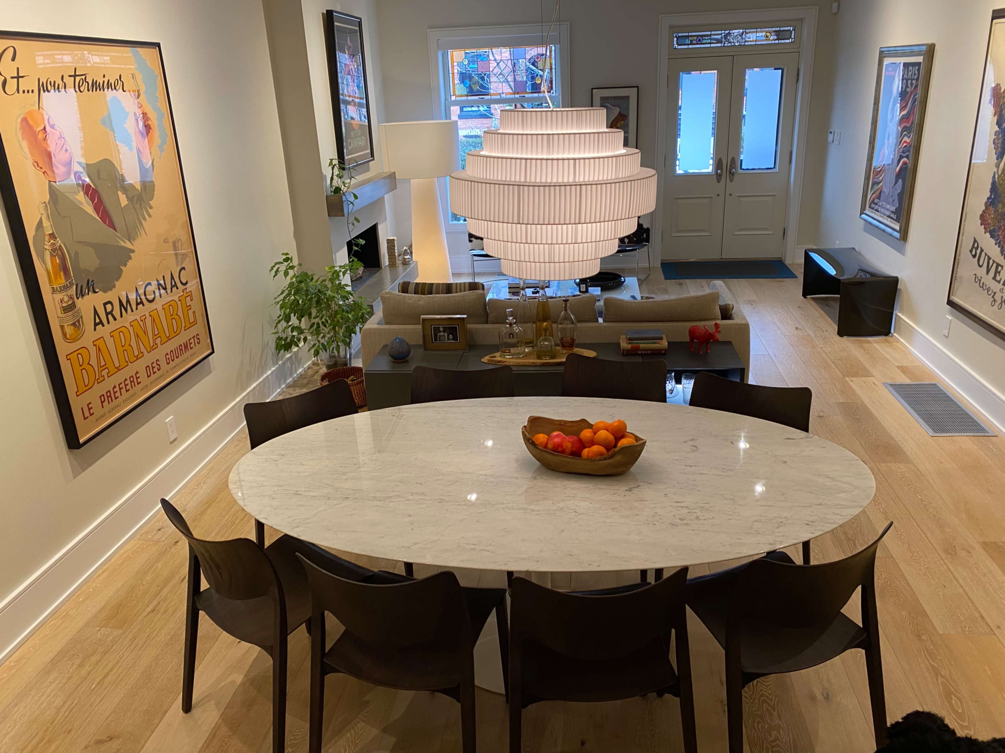 A modern dining area features a large oval marble table surrounded by dark wood chairs, with a pendant light and artwork on the walls.