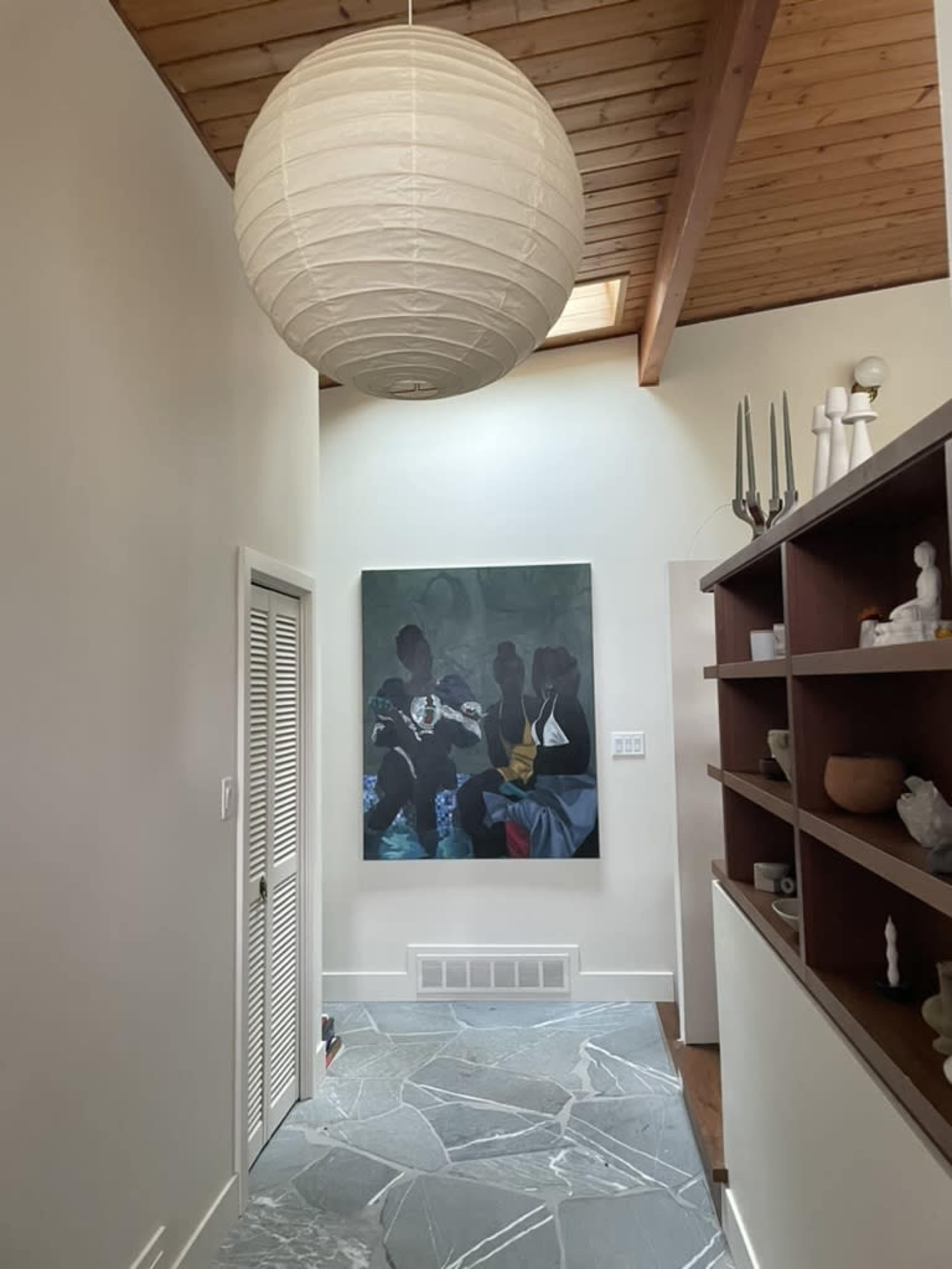 The image shows a hallway with a large artwork on the wall, a lantern-style light fixture above, and a bookshelf to the right.