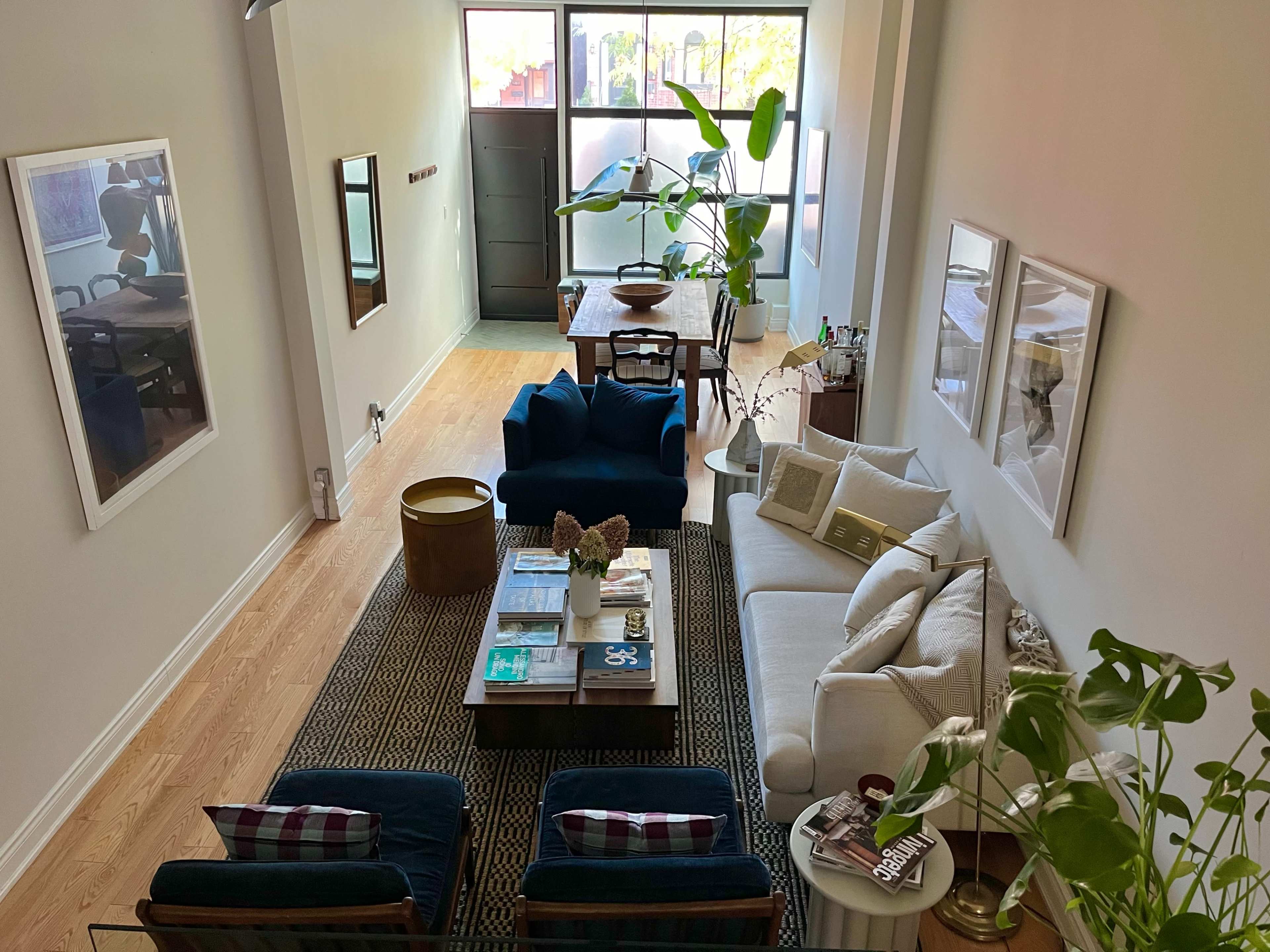 A spacious living room features a white sofa, blue armchairs, a wooden coffee table, and large windows allowing natural light.