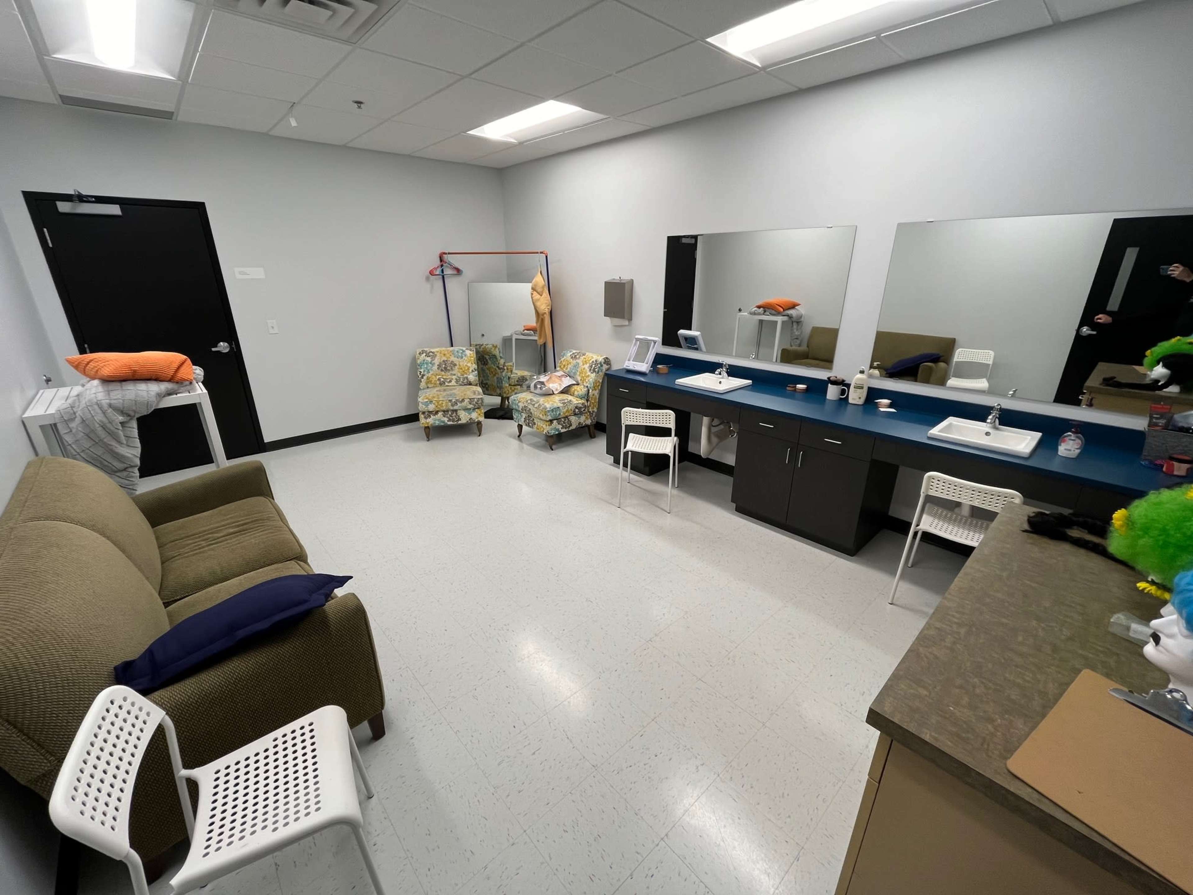 The image shows a small, sparsely furnished room with a couch, two chairs, a table with mirrors, and a mannequin in the corner.