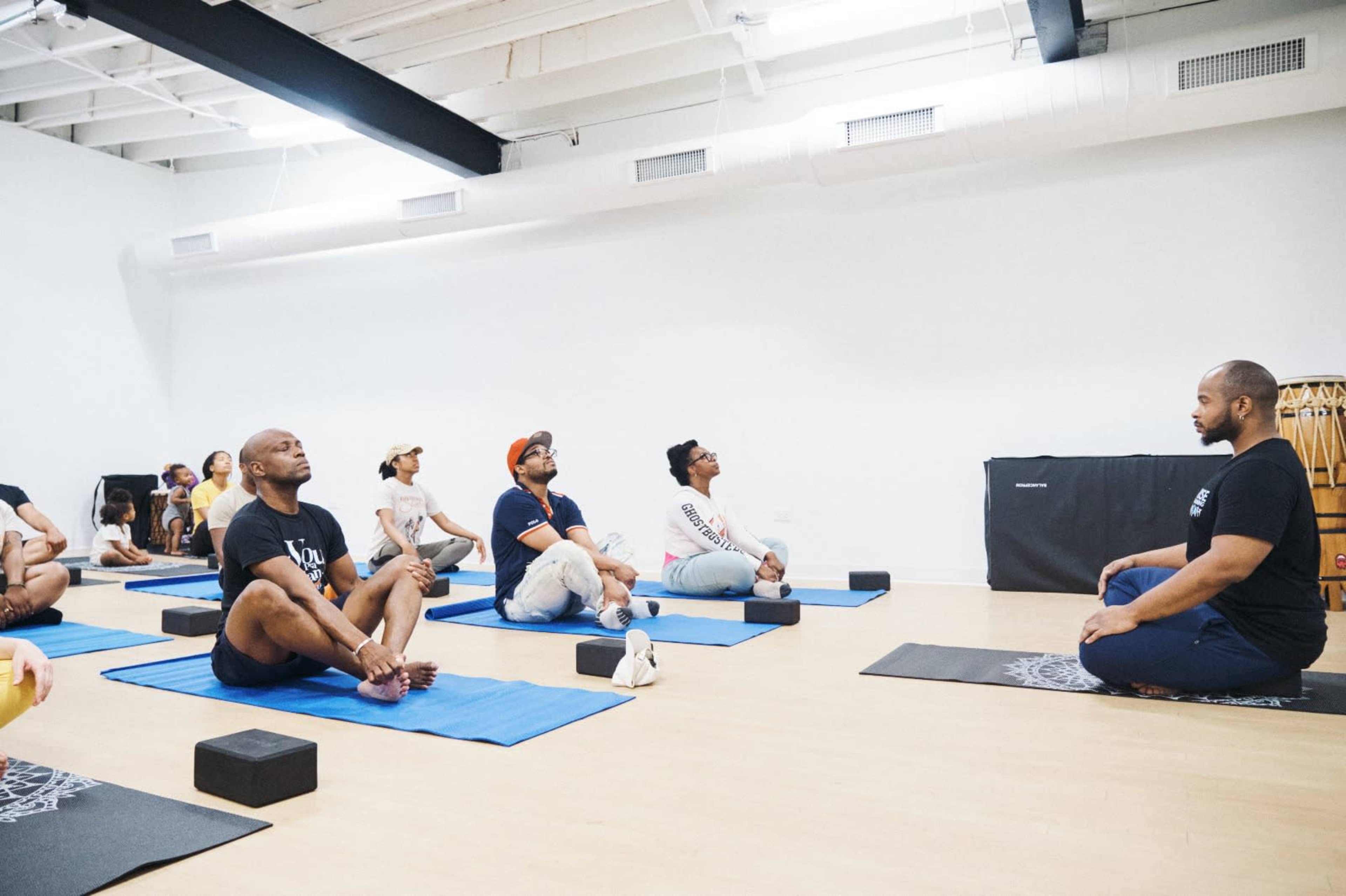 A group of people participates in a yoga class on blue mats in a spacious studio.