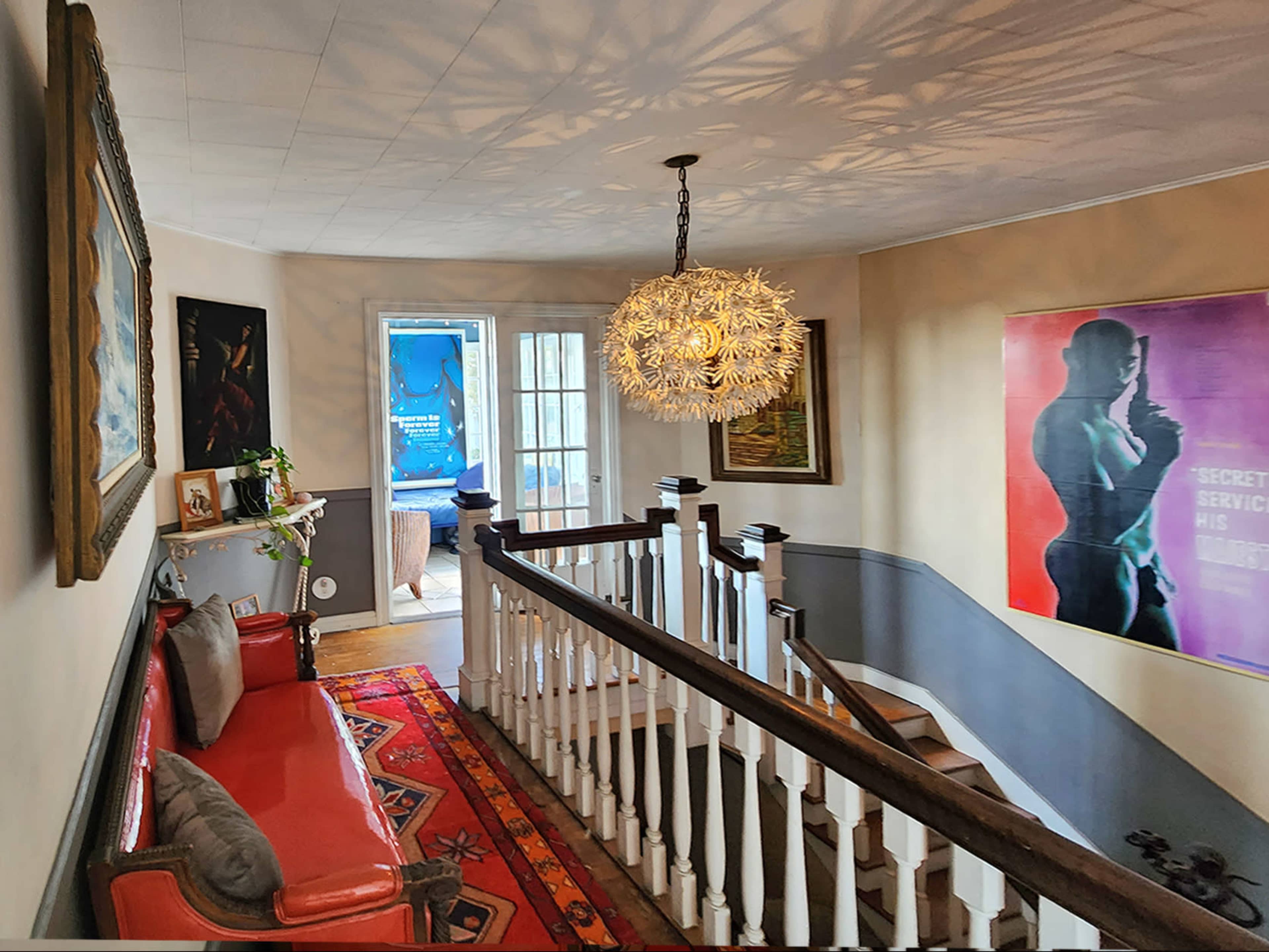 A hallway with a staircase, featuring a red sofa, a patterned rug, and a chandelier casting intricate shadows on the walls.