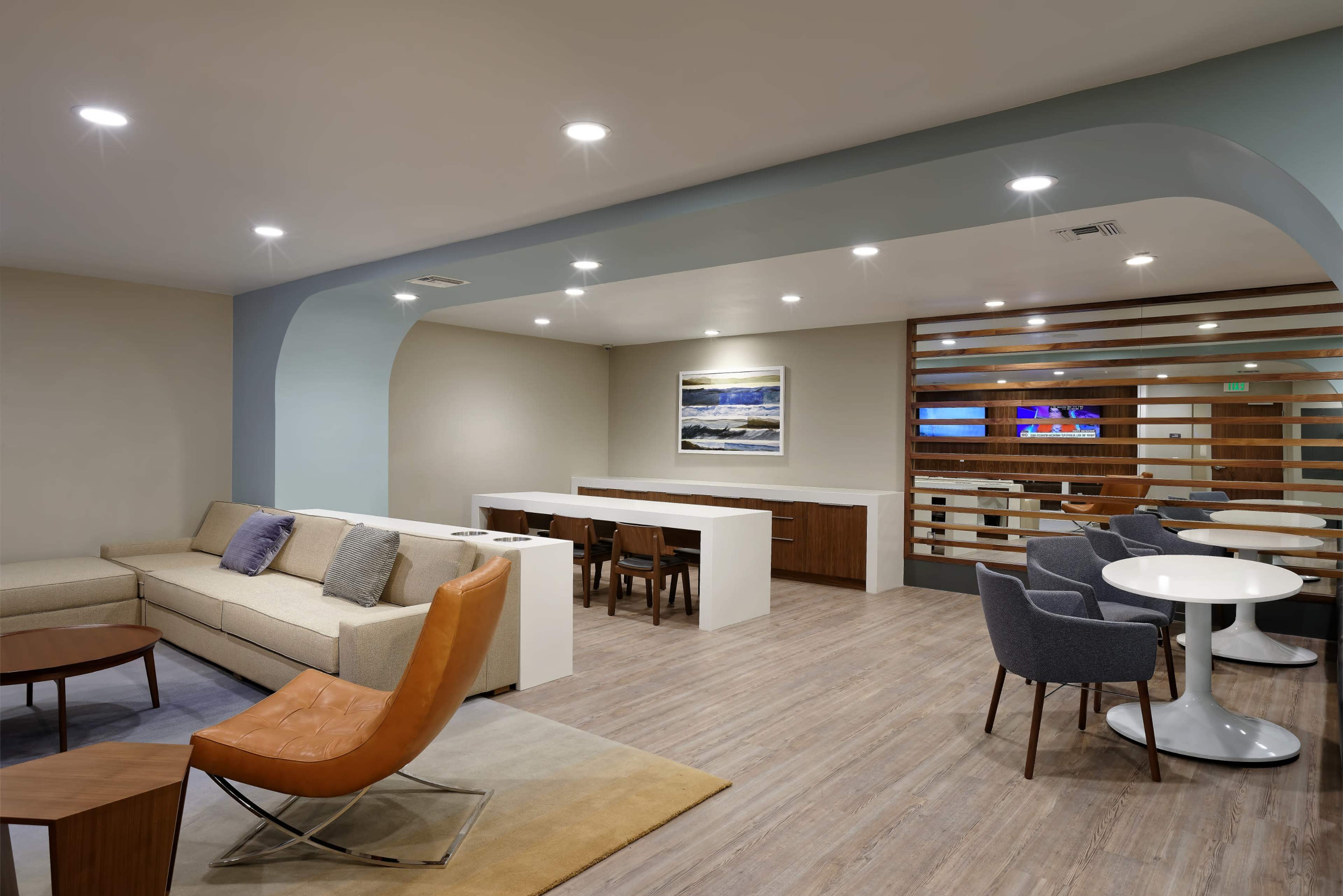 A modern lounge area with a sofa, chairs, and tables, featuring a light-colored wooden floor and subtle lighting.