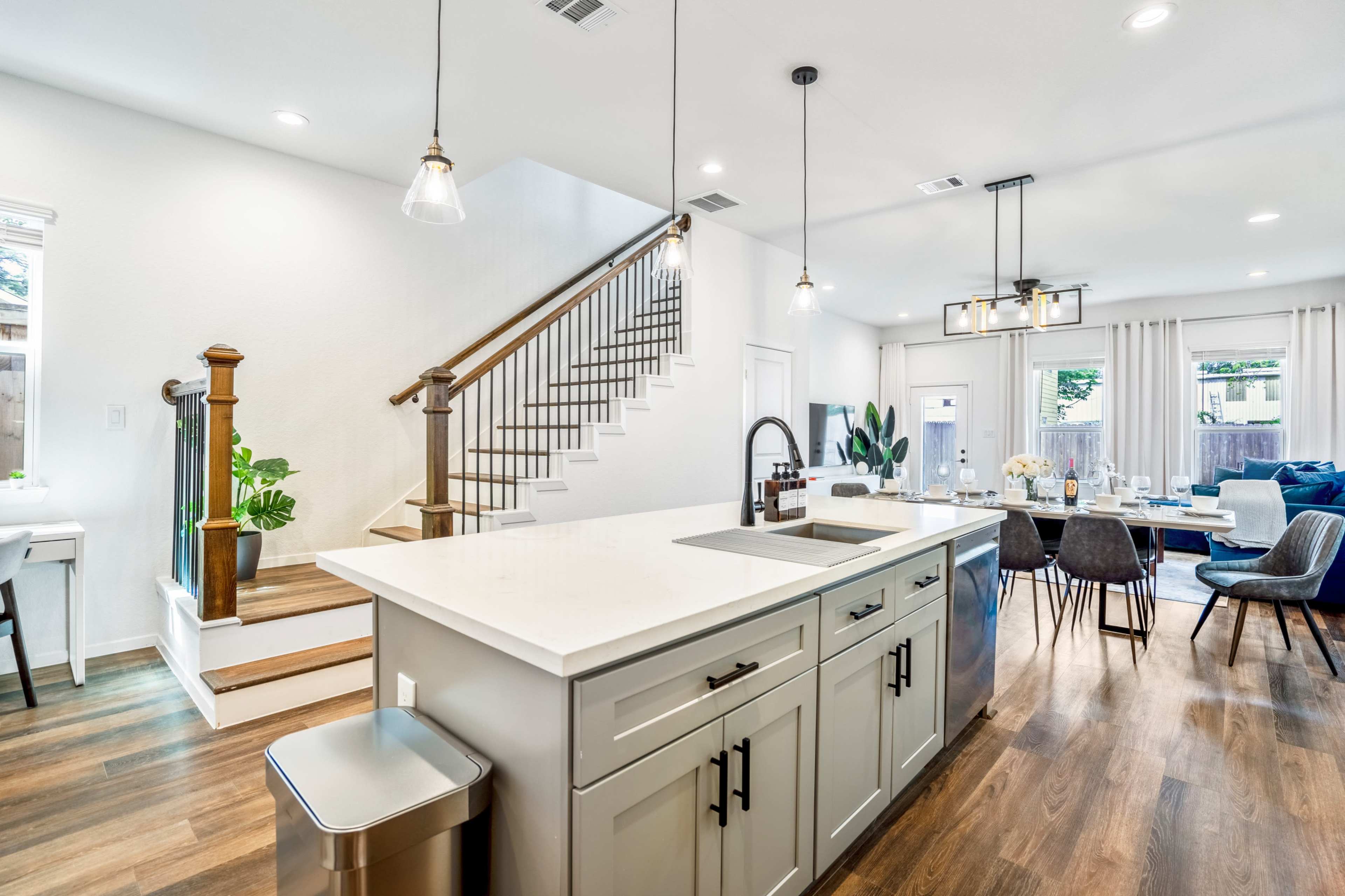 A modern kitchen features an island with a sink, surrounded by a dining area and a staircase leading to an upper floor.