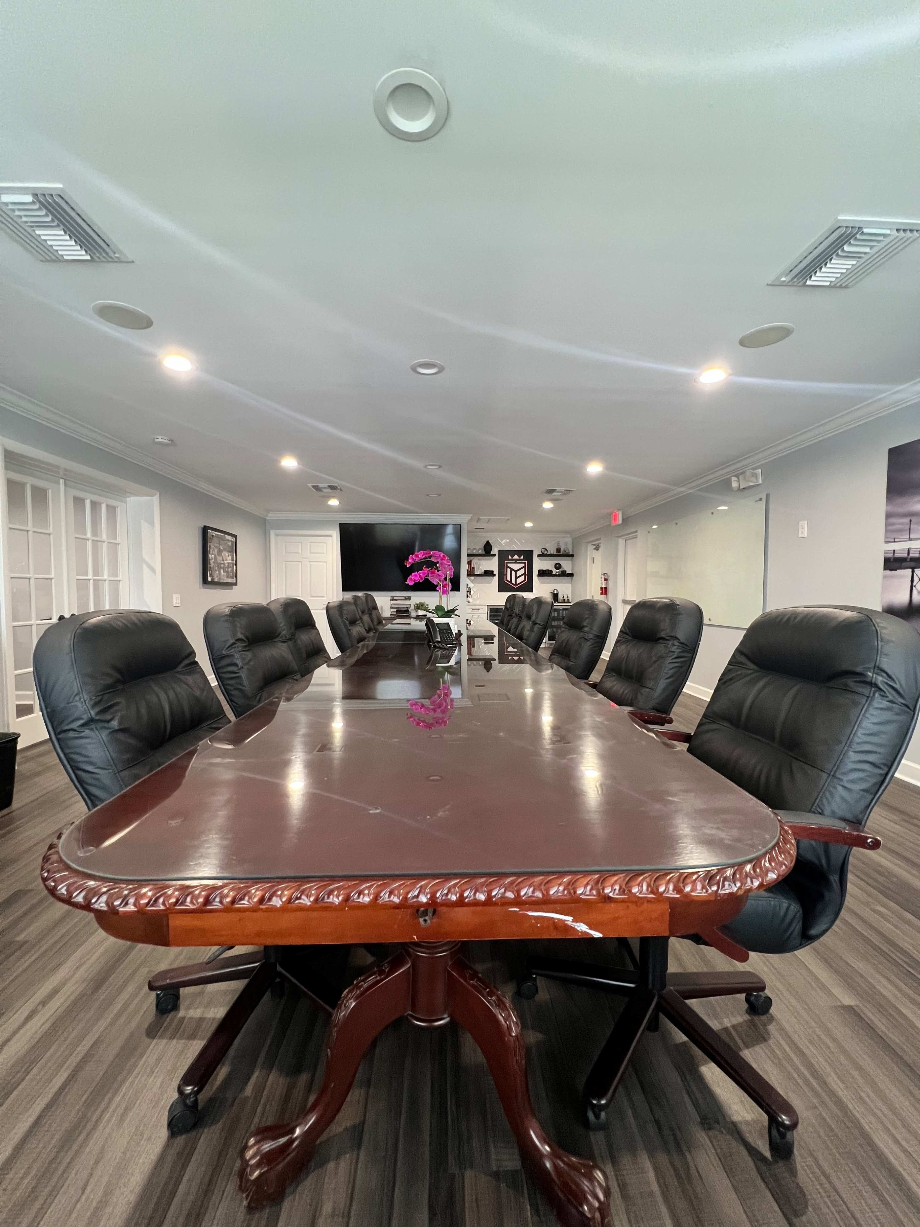 A large conference room features a wooden table surrounded by black leather office chairs.