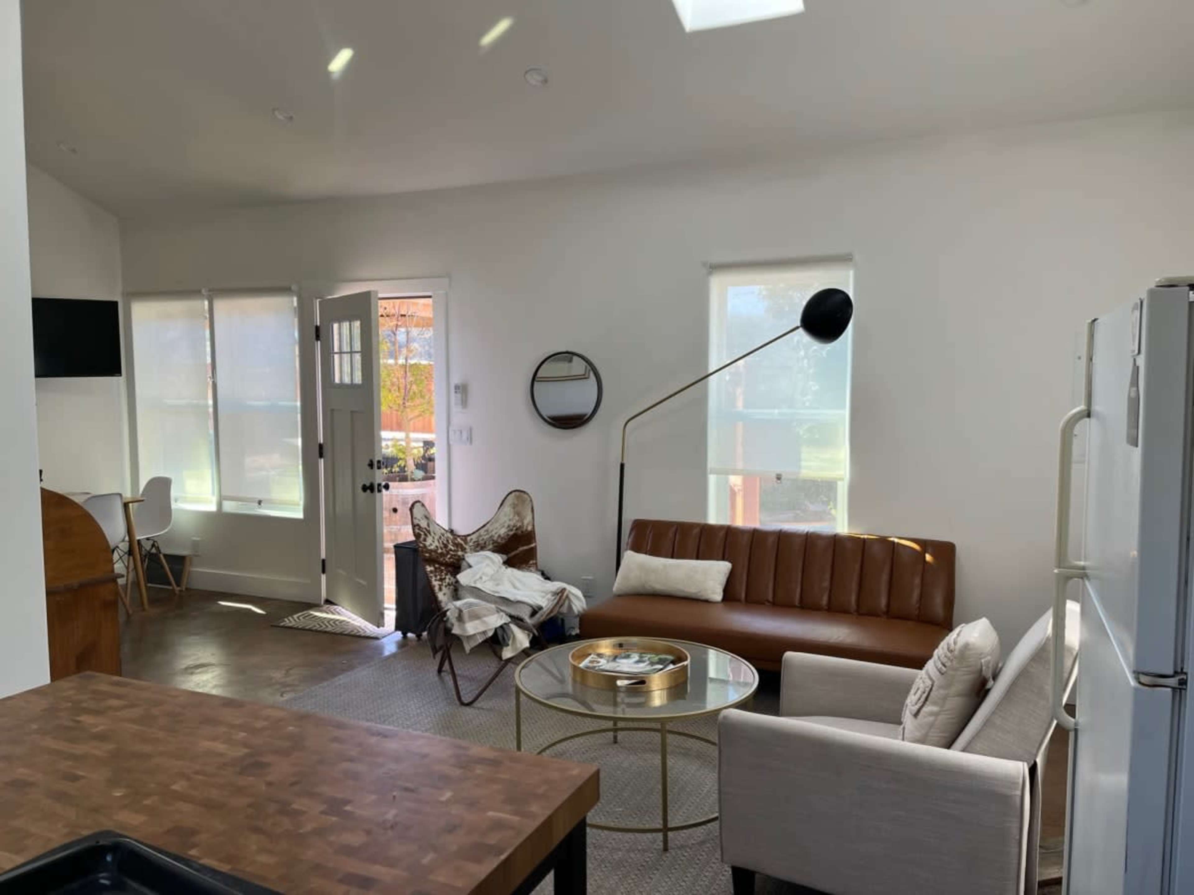 The image shows a modern living room with a brown couch, a round coffee table, and large windows that open to a patio area.