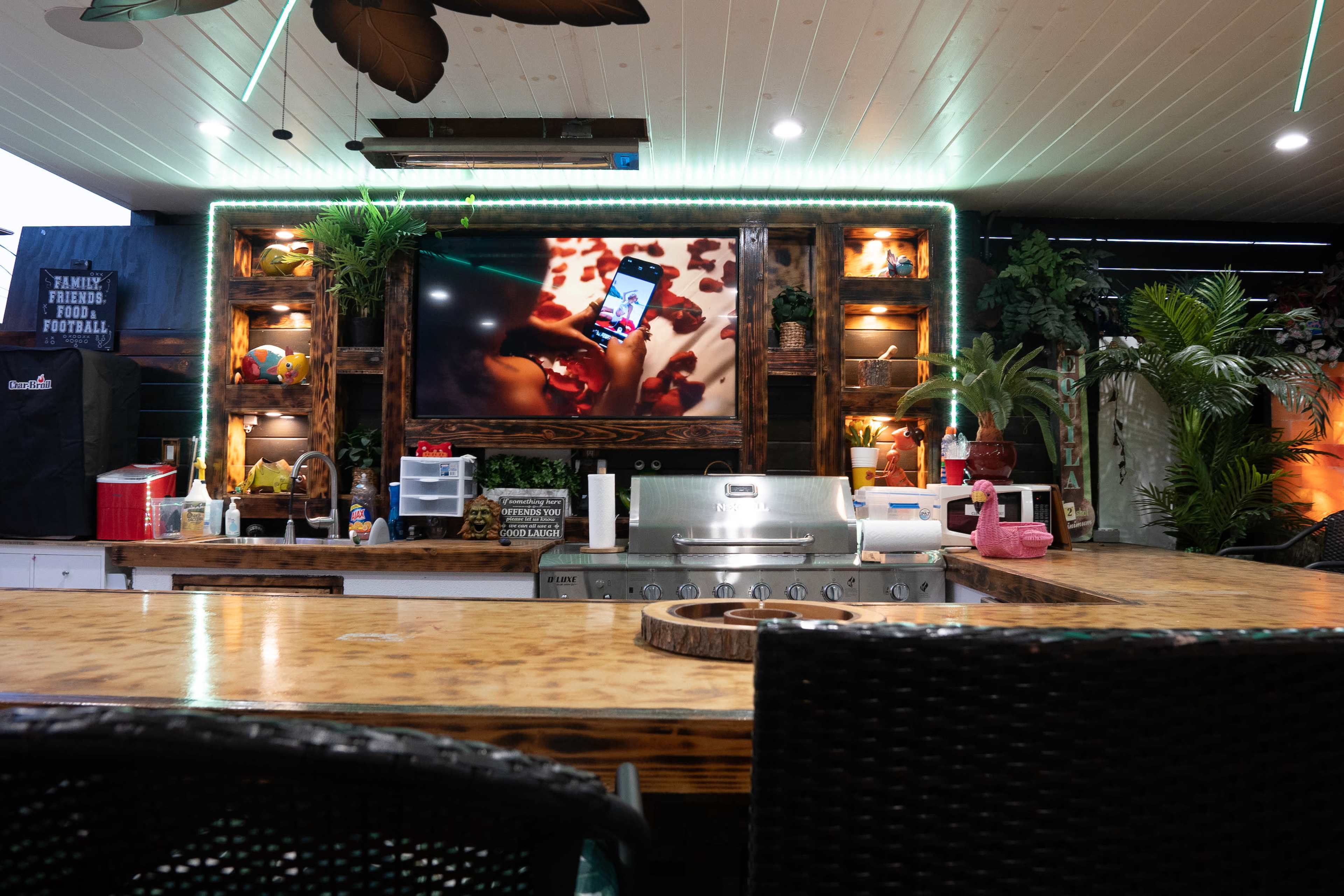 An outdoor kitchen area featuring a large grill, a television displaying a video, and various tropical decor elements.