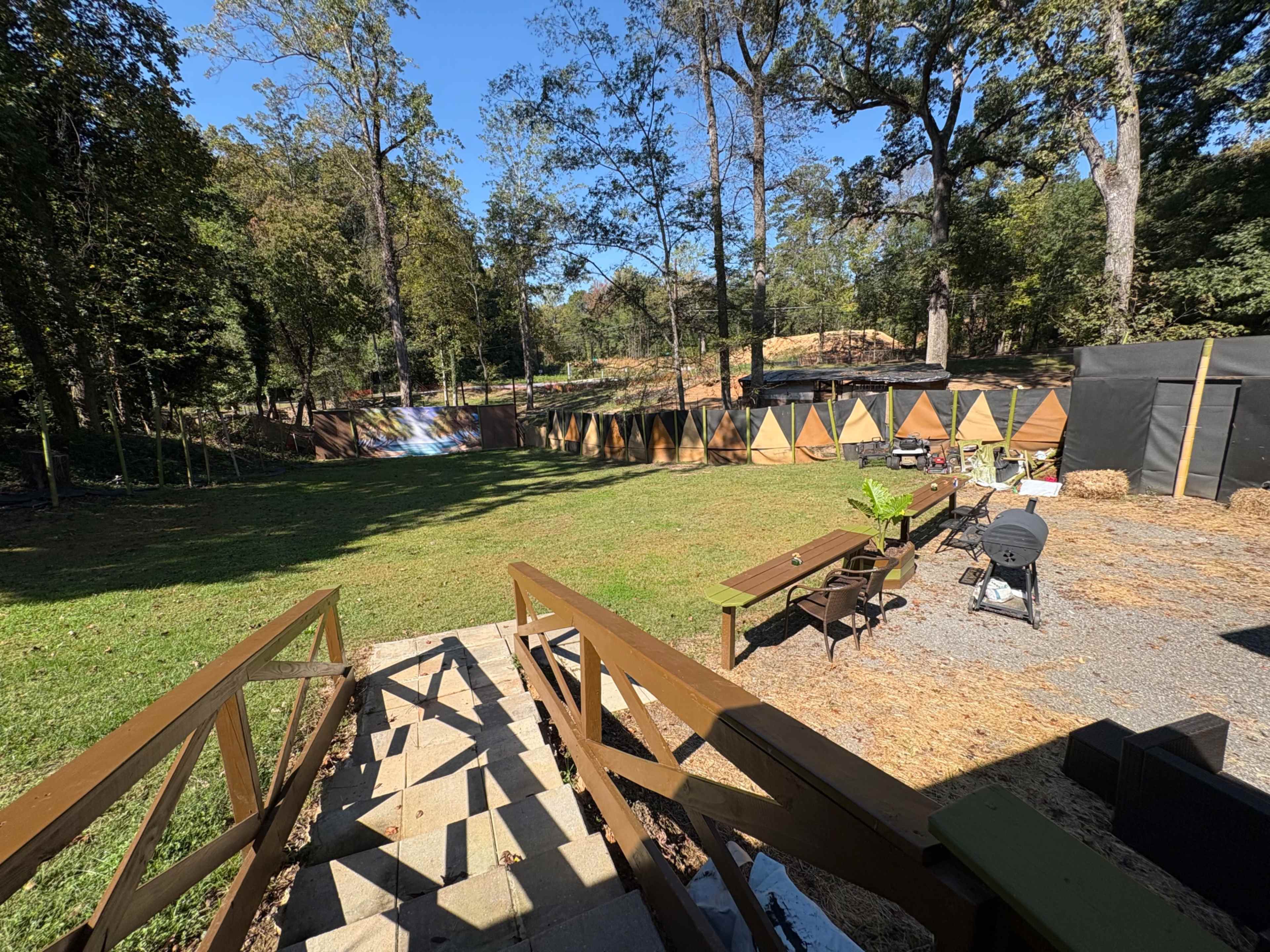 The image shows a landscaped backyard with a set of wooden steps leading down to a grassy area, surrounded by trees and a fence with triangular panels in the background.