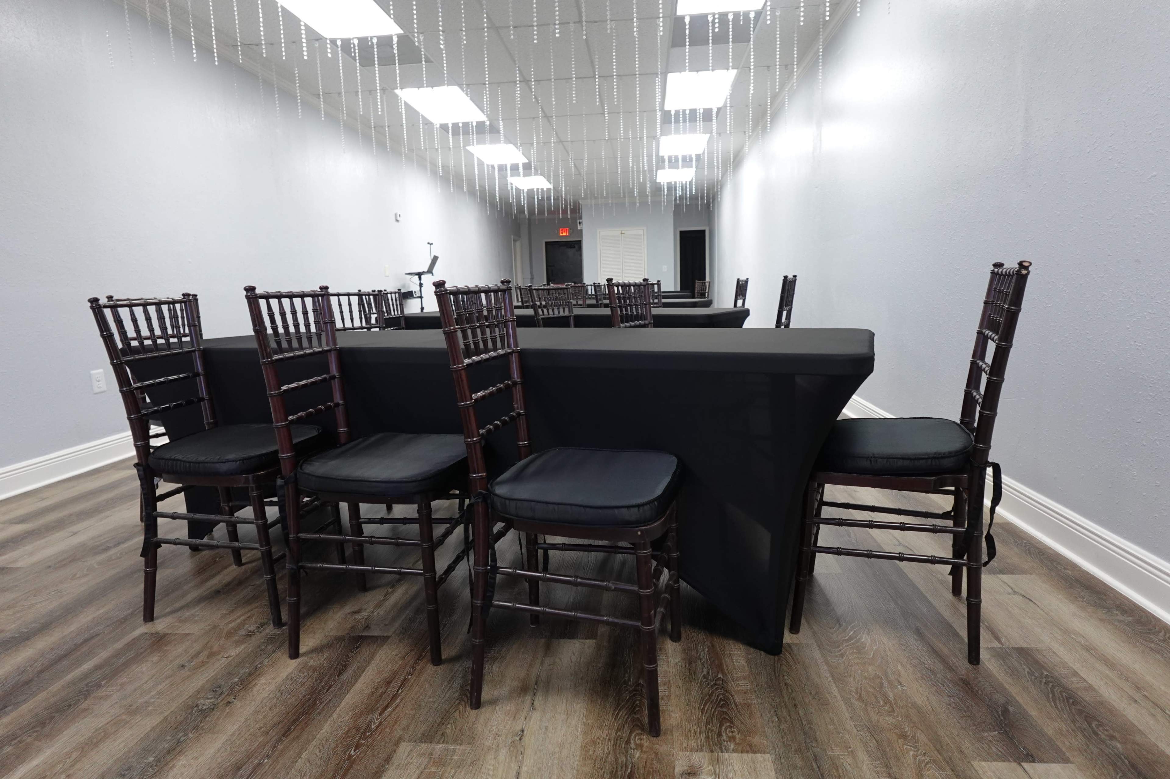 A spacious, poorly lit event room with rows of dark tables and wooden chairs arranged for a gathering.