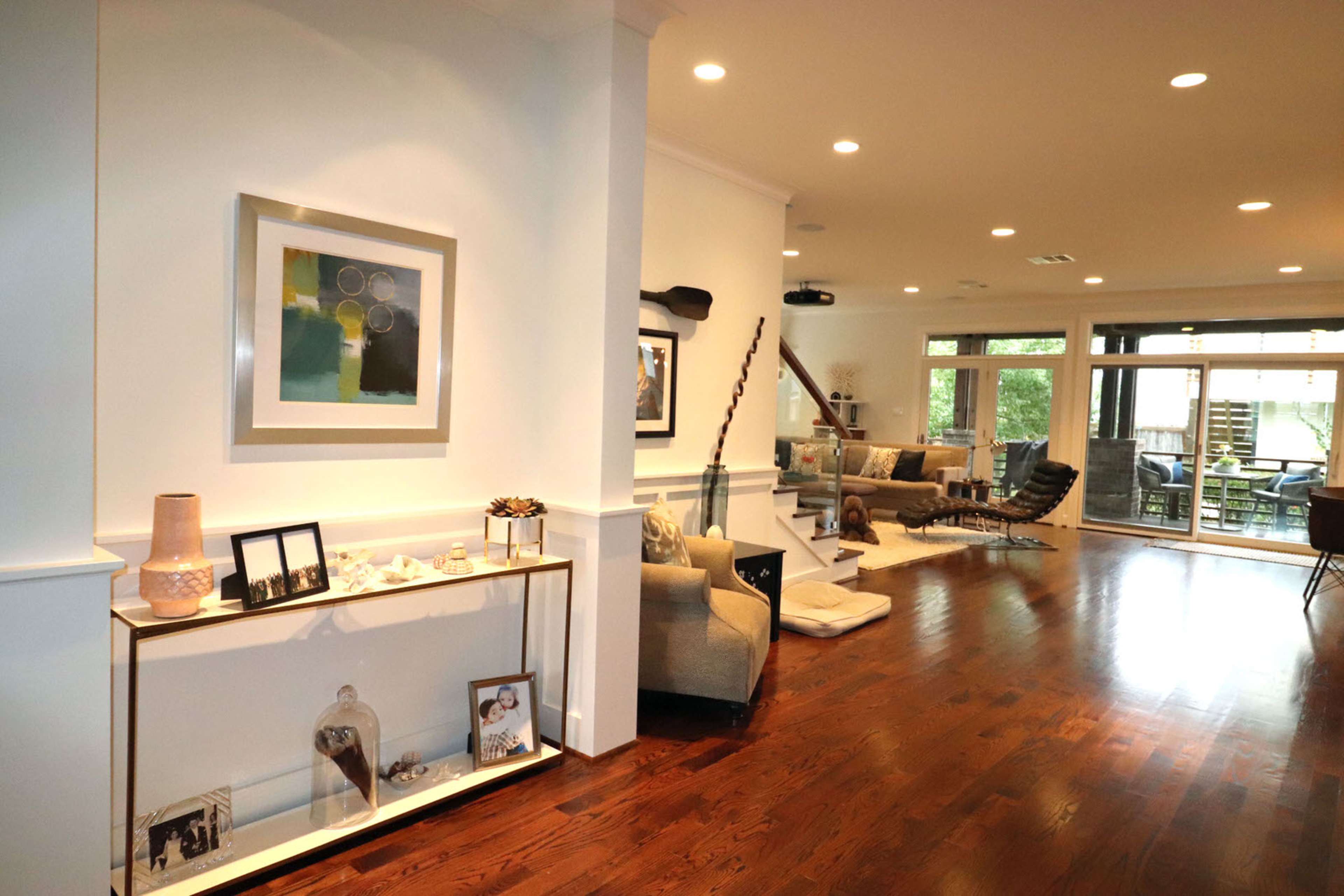 A spacious living area with wooden flooring, modern furniture, and large windows that open to a patio.