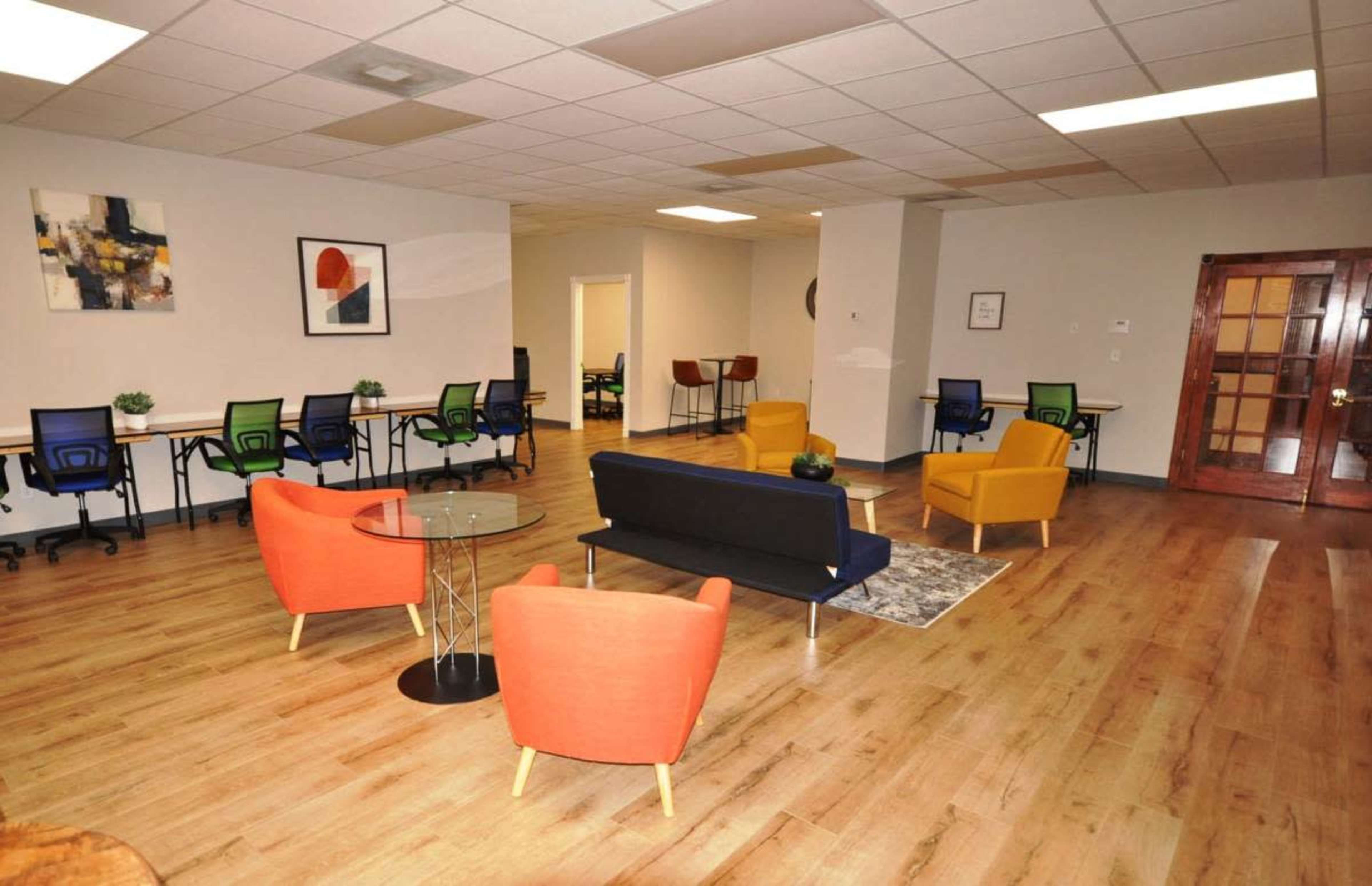 The image shows a modern office space with several workstations, seating areas, and wooden flooring.