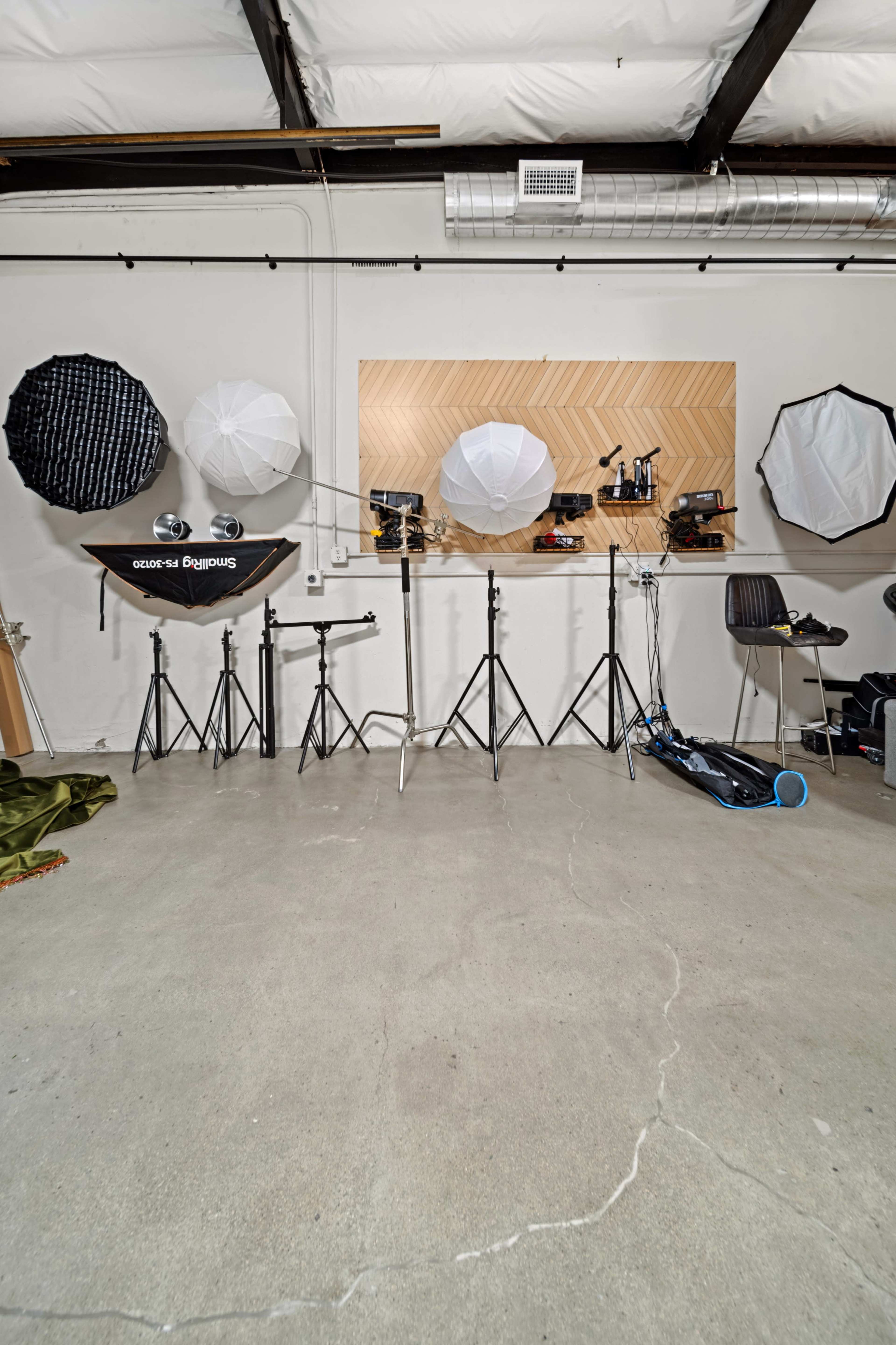The image shows a photography studio setup with various light modifiers mounted on stands against a wall with a wood-patterned panel.