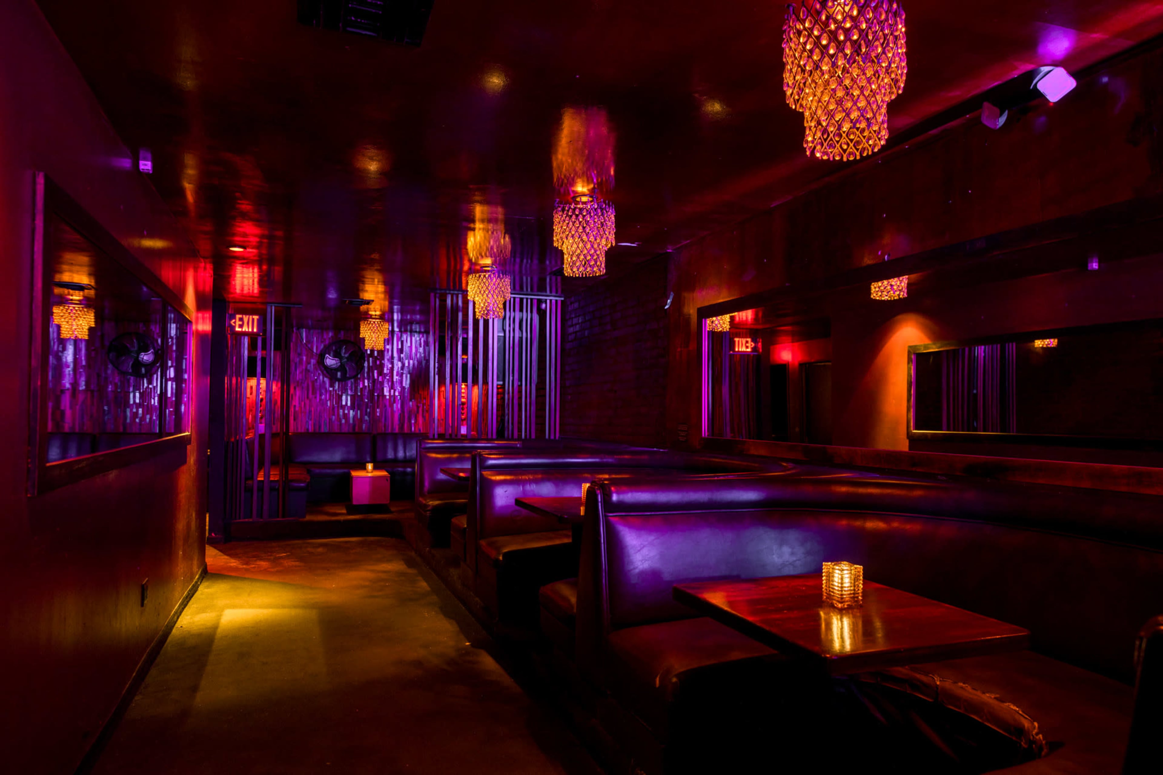 A dimly lit lounge with dark seating, vibrant purple lighting, and decorative chandeliers.