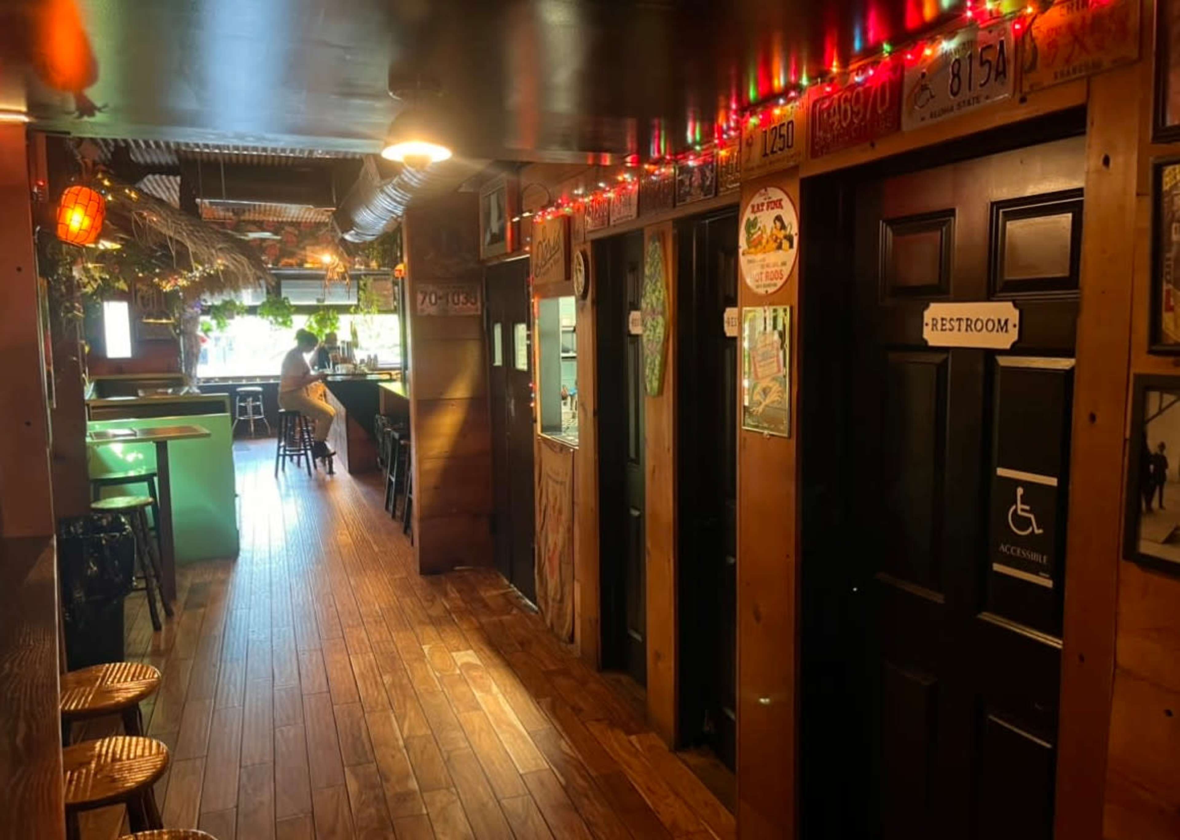 A narrow hallway in a restaurant with wooden floors, decorated with string lights and featuring several closed doors, including one labeled "RESTROOM."