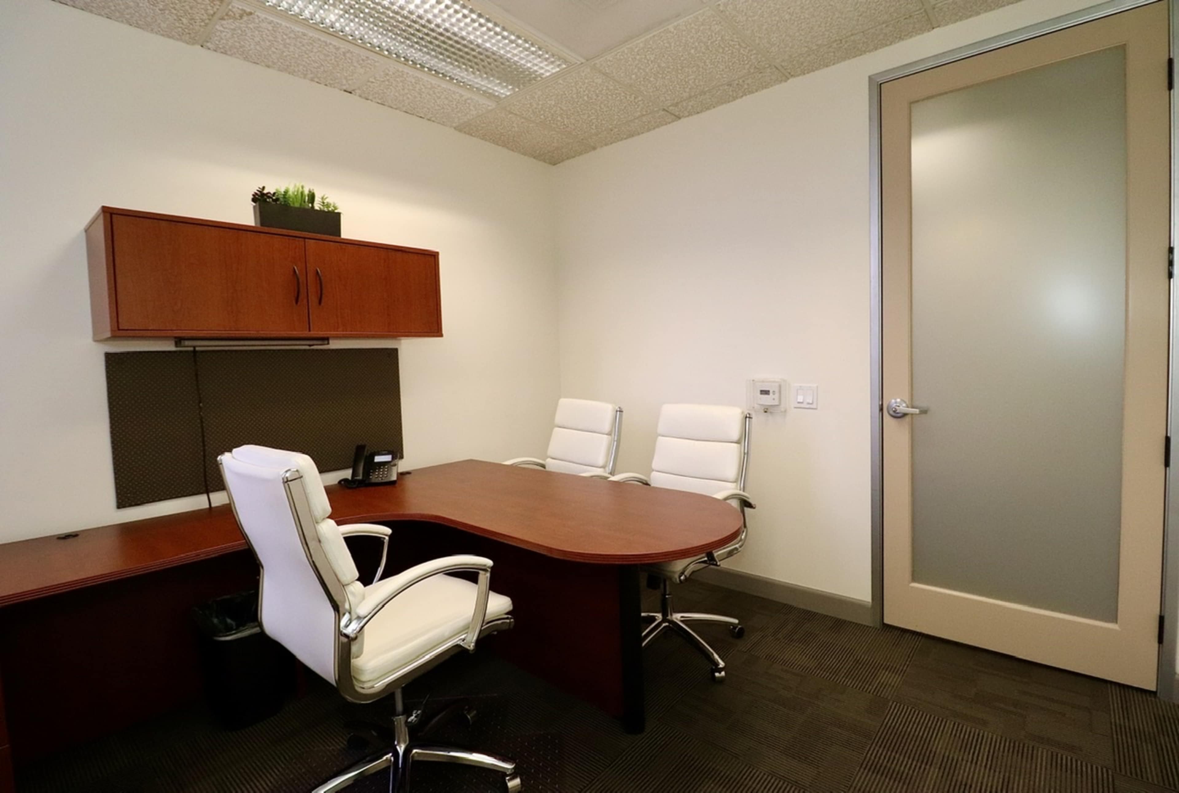 A small office with a wooden desk, two white chairs, and a door leading outside.