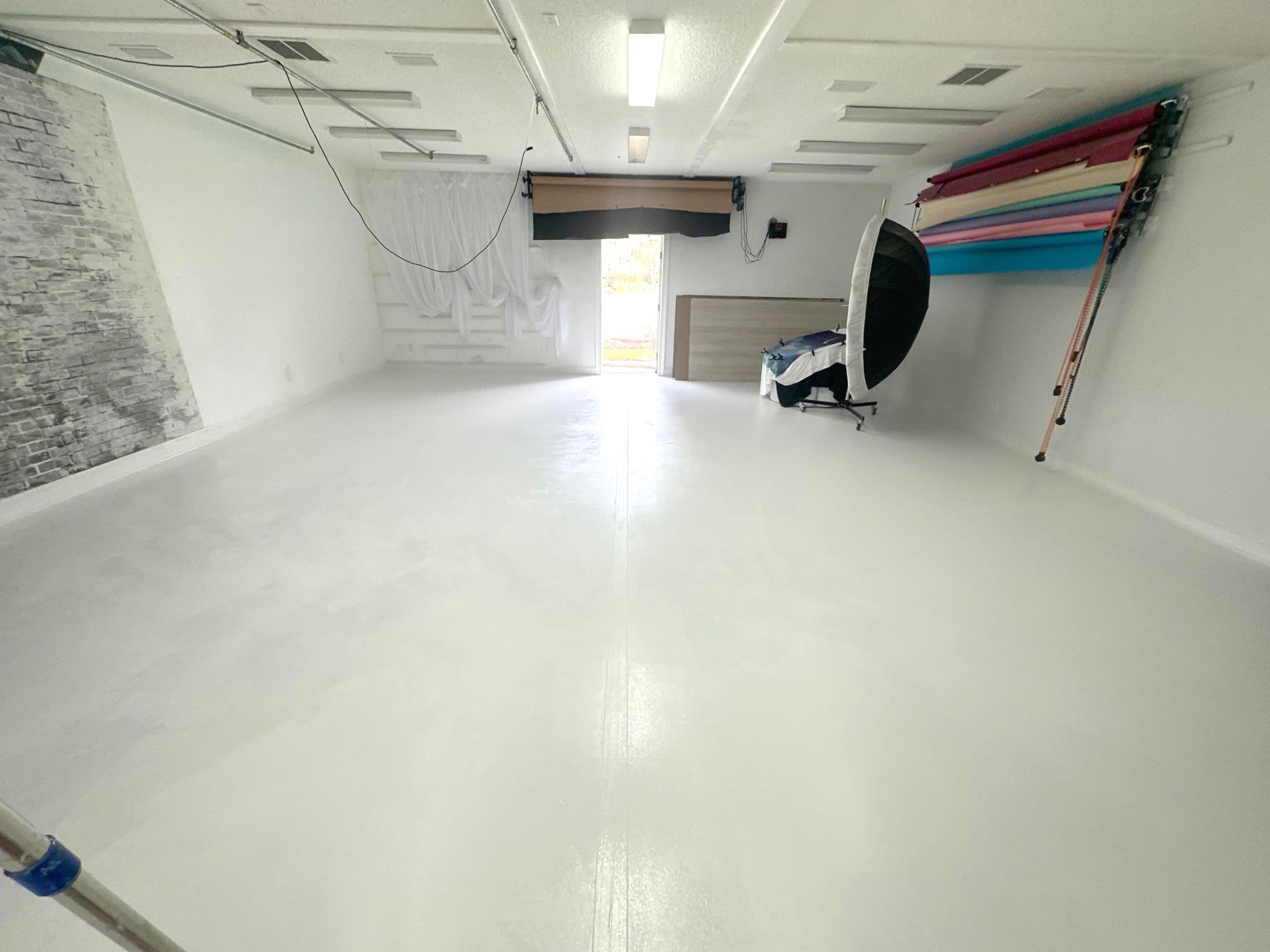 A large, empty, well-lit room with a smooth white floor and a backdrop stand against one wall.