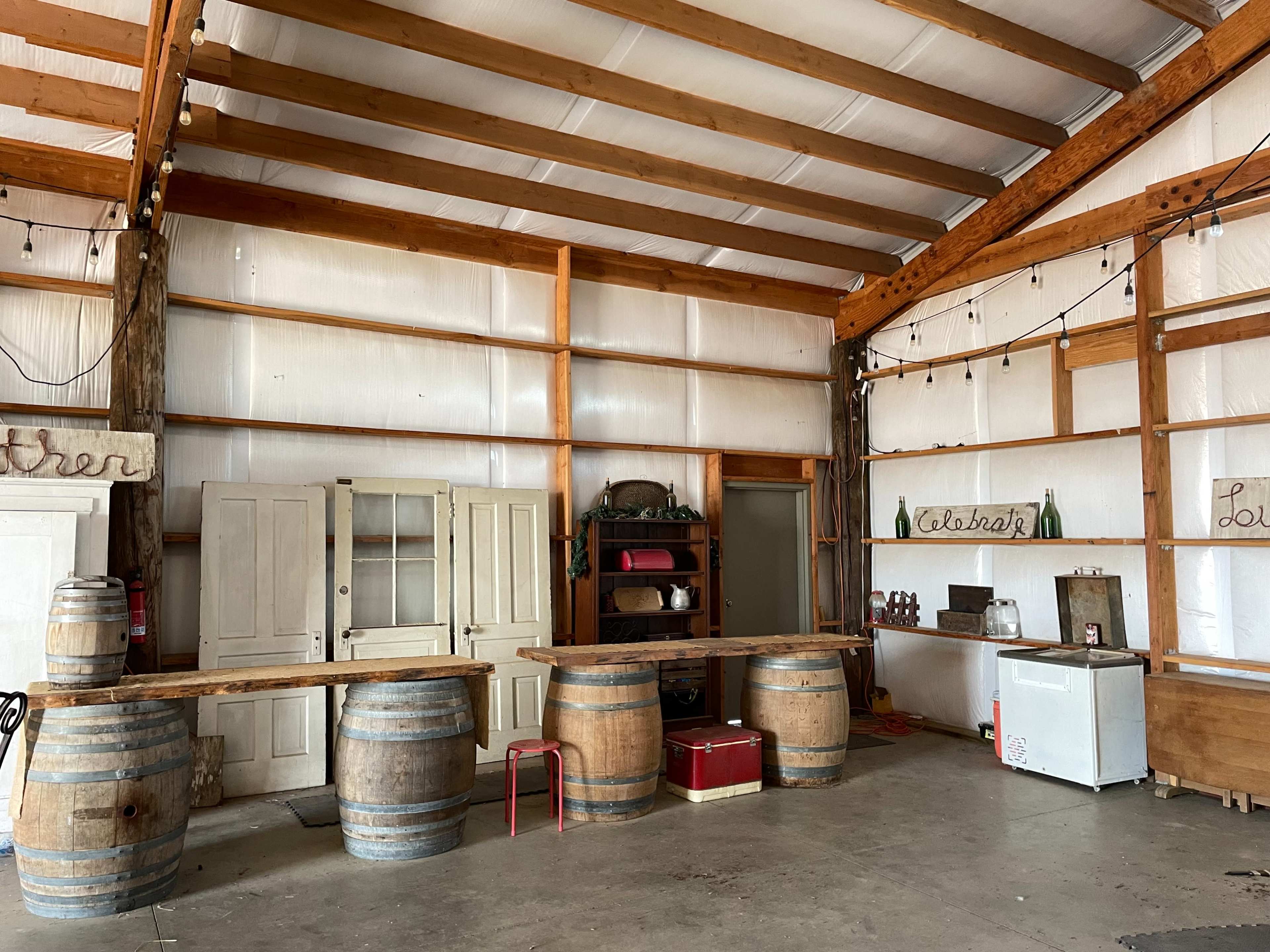 The interior of a spacious building features a wooden bar made from barrels, with vintage decor and furniture along the walls.
