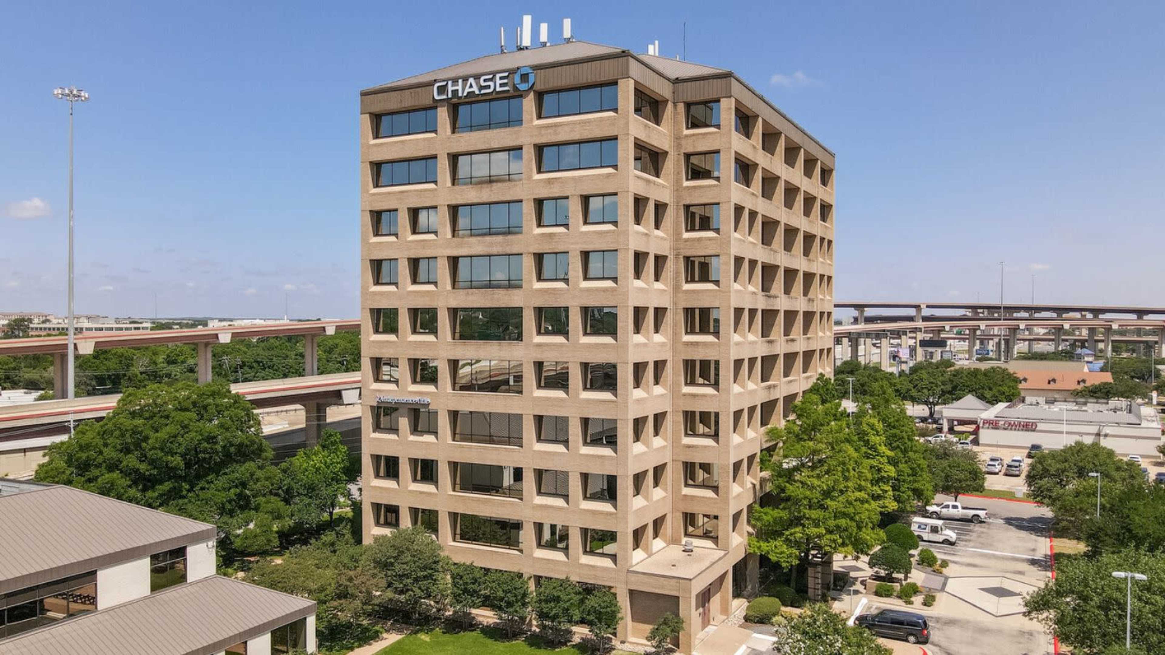 A multi-story office building with the Chase logo prominently displayed on its rooftop, surrounded by trees and parking areas.