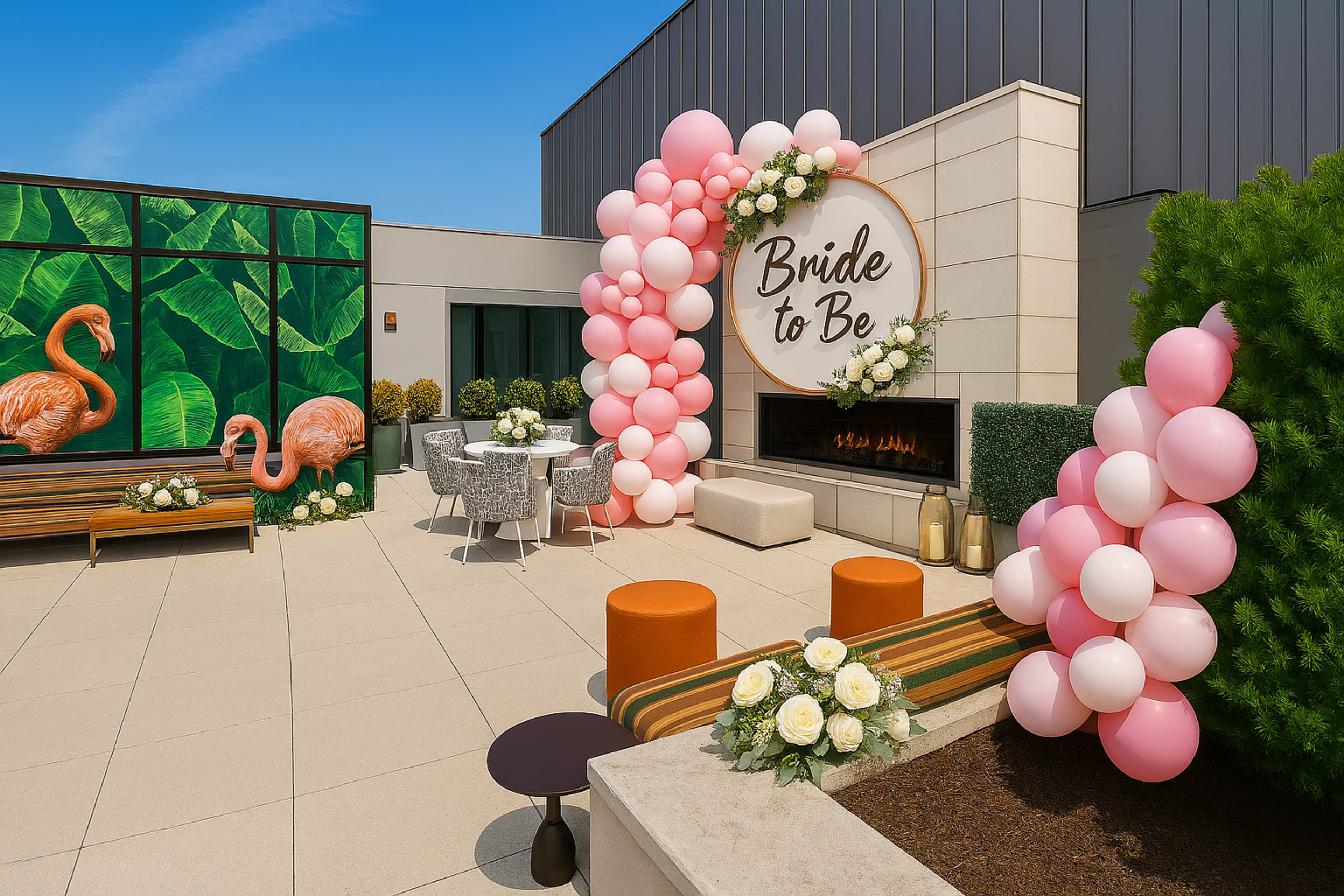 The image shows an outdoor event space decorated with pink and white balloons, floral arrangements, and modern seating, featuring a "Bride to Be" sign.