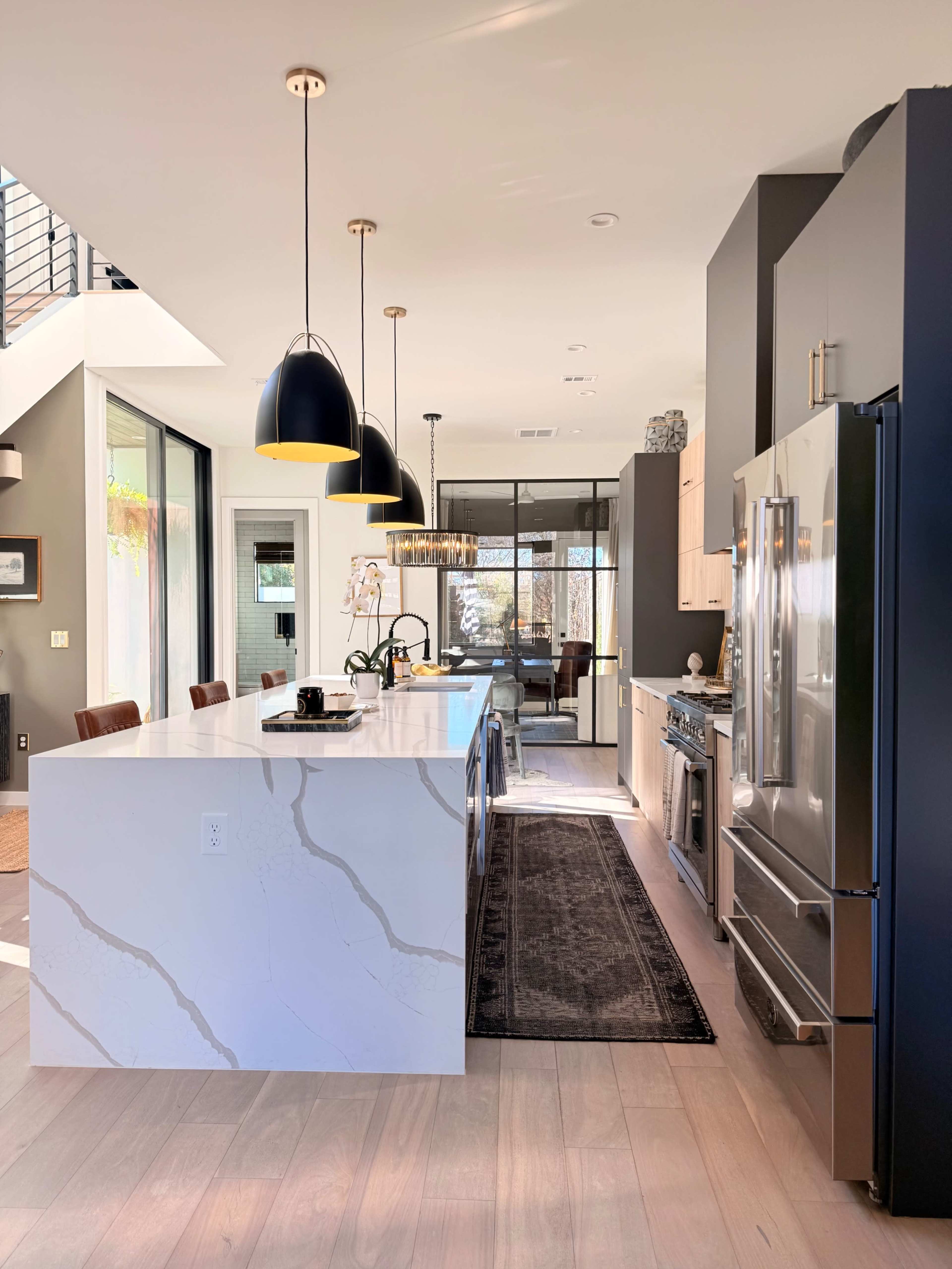 The image shows a modern kitchen with a large island, sleek cabinetry, and pendant lights above.