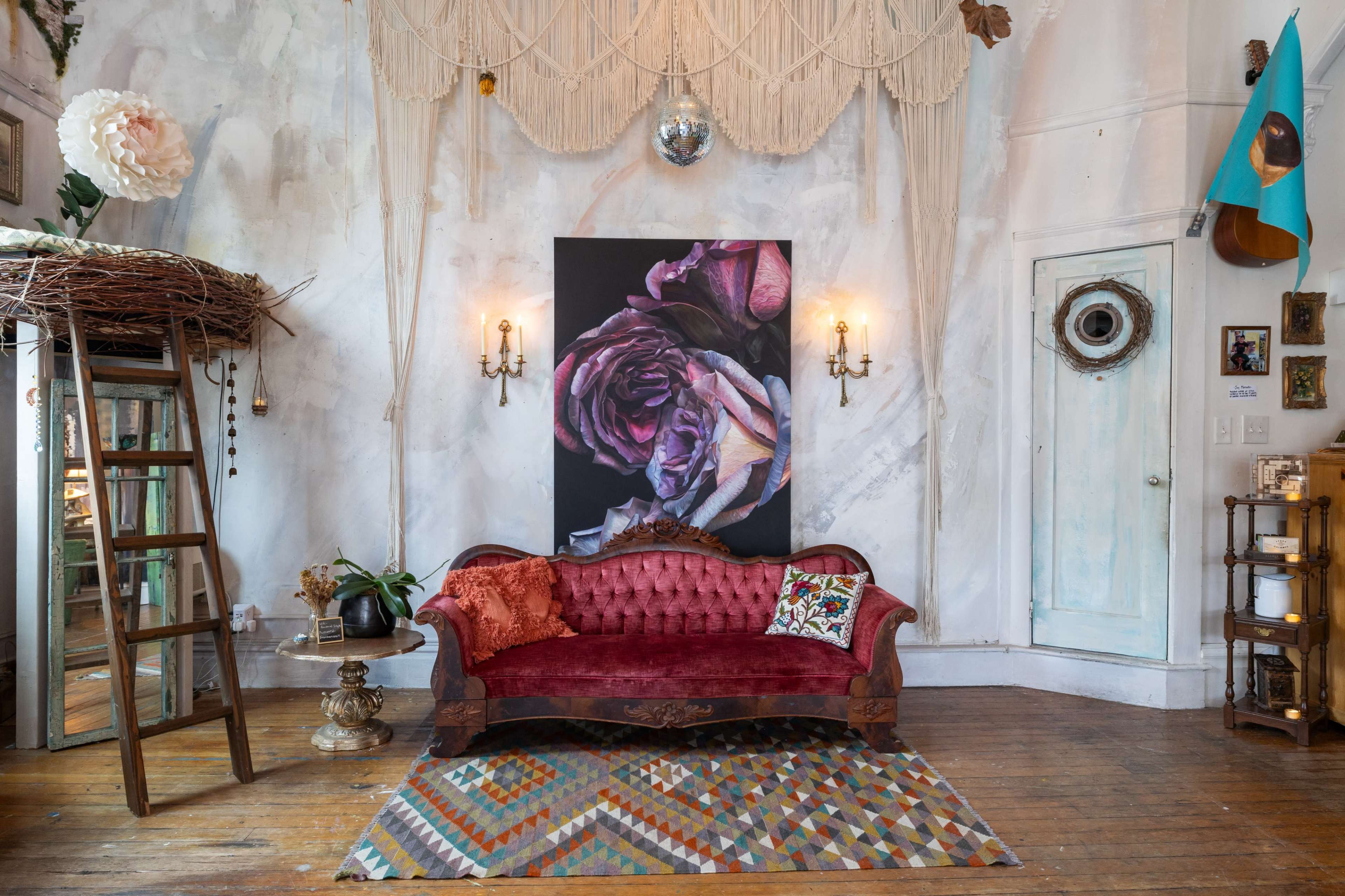The image features a vintage living room with a red upholstered sofa, a large floral painting on the wall, and eclectic decorative elements, including a mirror and a patterned rug.
