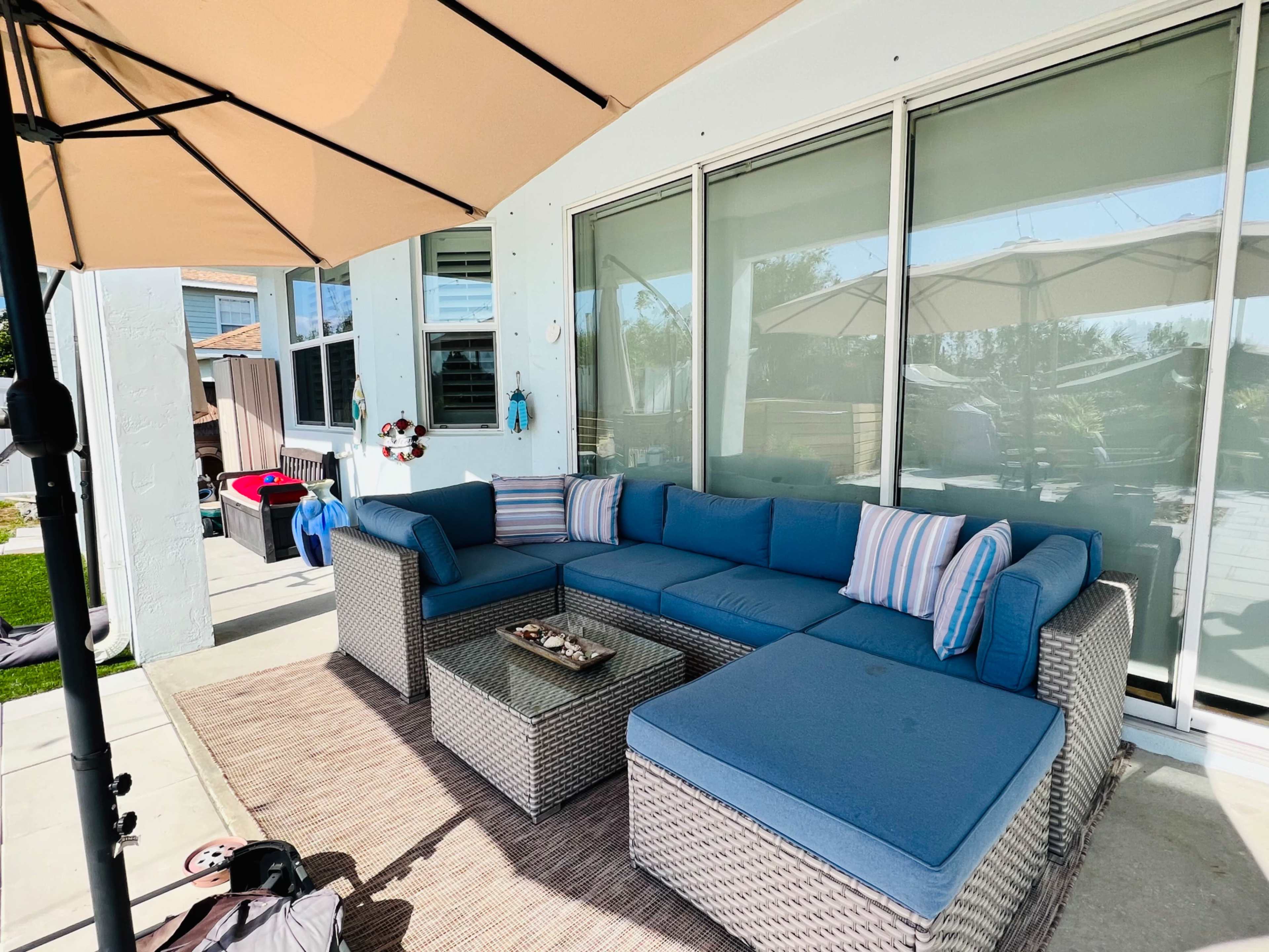 The image shows a spacious outdoor seating area featuring a blue sectional sofa, a glass-topped table, and an umbrella providing shade.